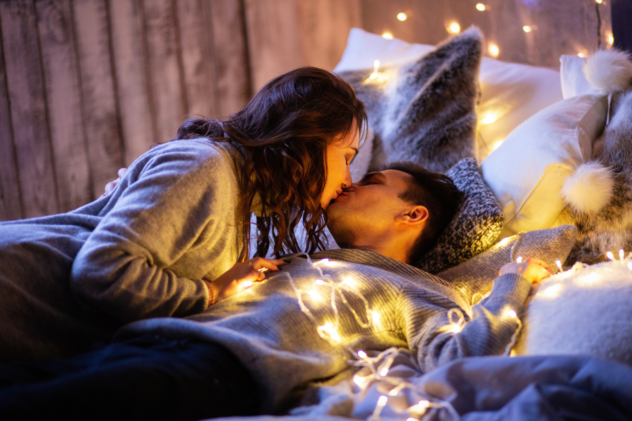 девушка  и молодой человек  лежат на кровати. они  обмотаны  гирляндой