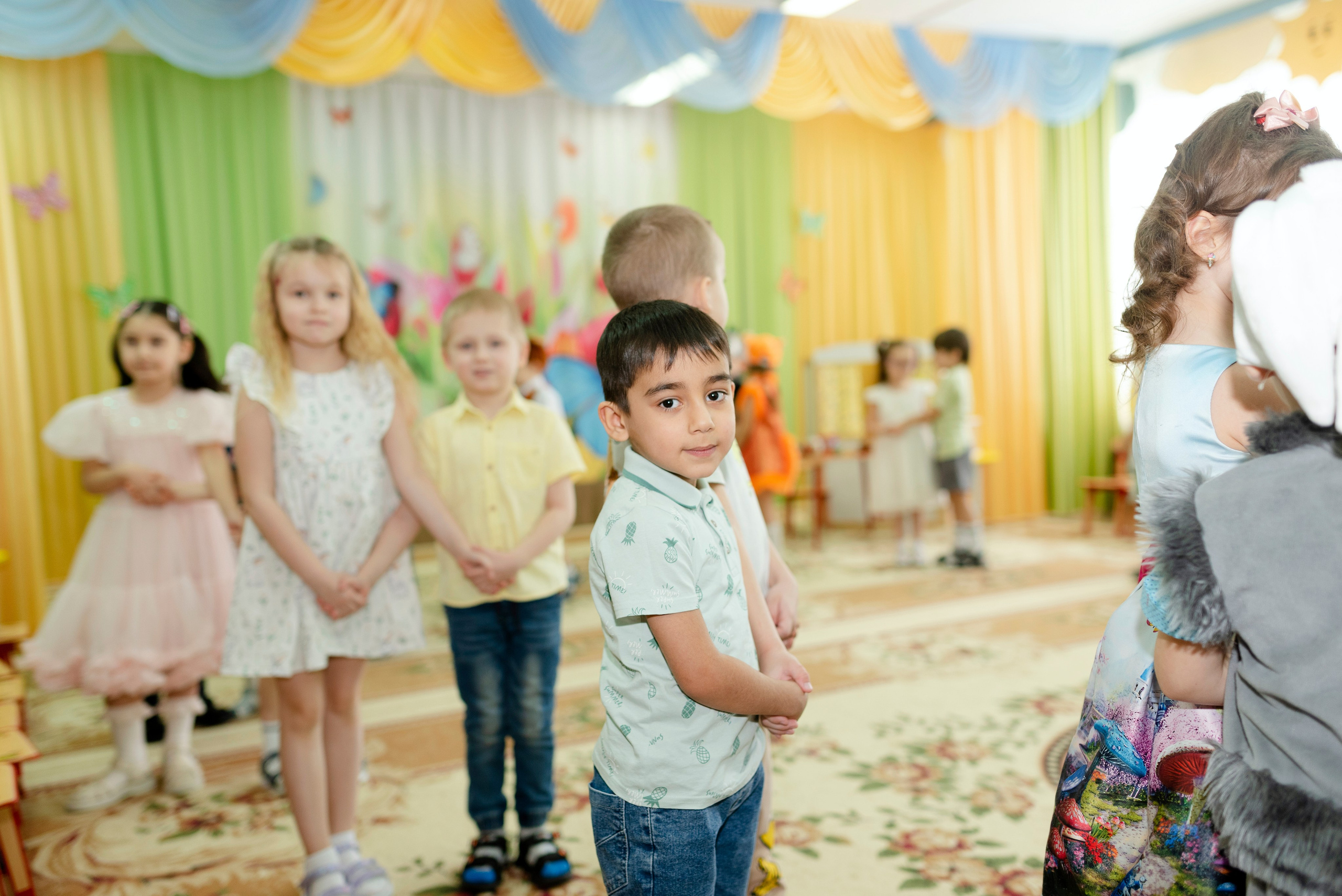 Дети танцуют веселый танец в праздничных костюмах на утреннике 8 марта в детском саду.