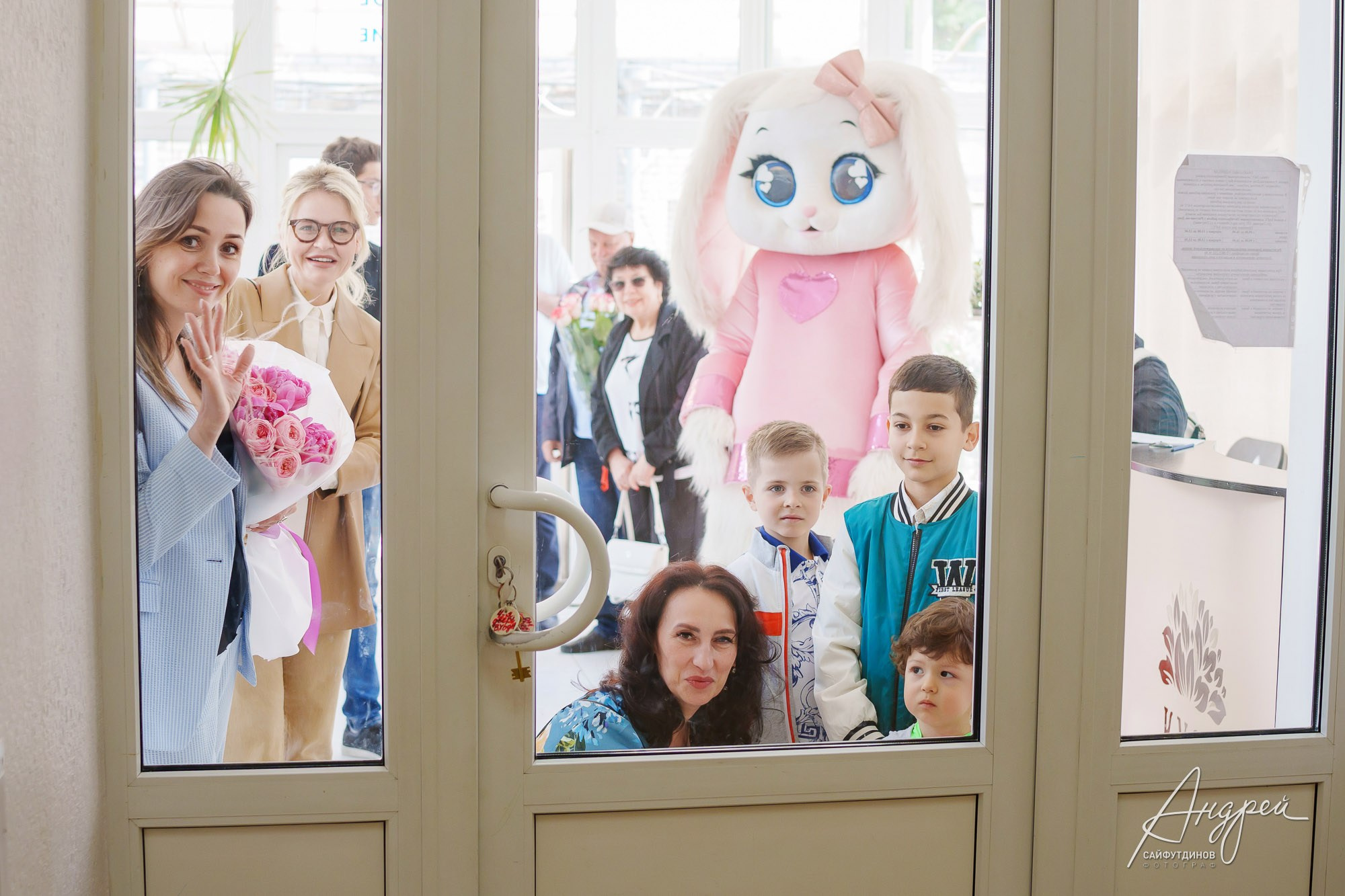 Гости и родственники смотрят в дверное стекло пеленальной комнаты роддома, фотограф на выписку в Ростове-на-Дону.