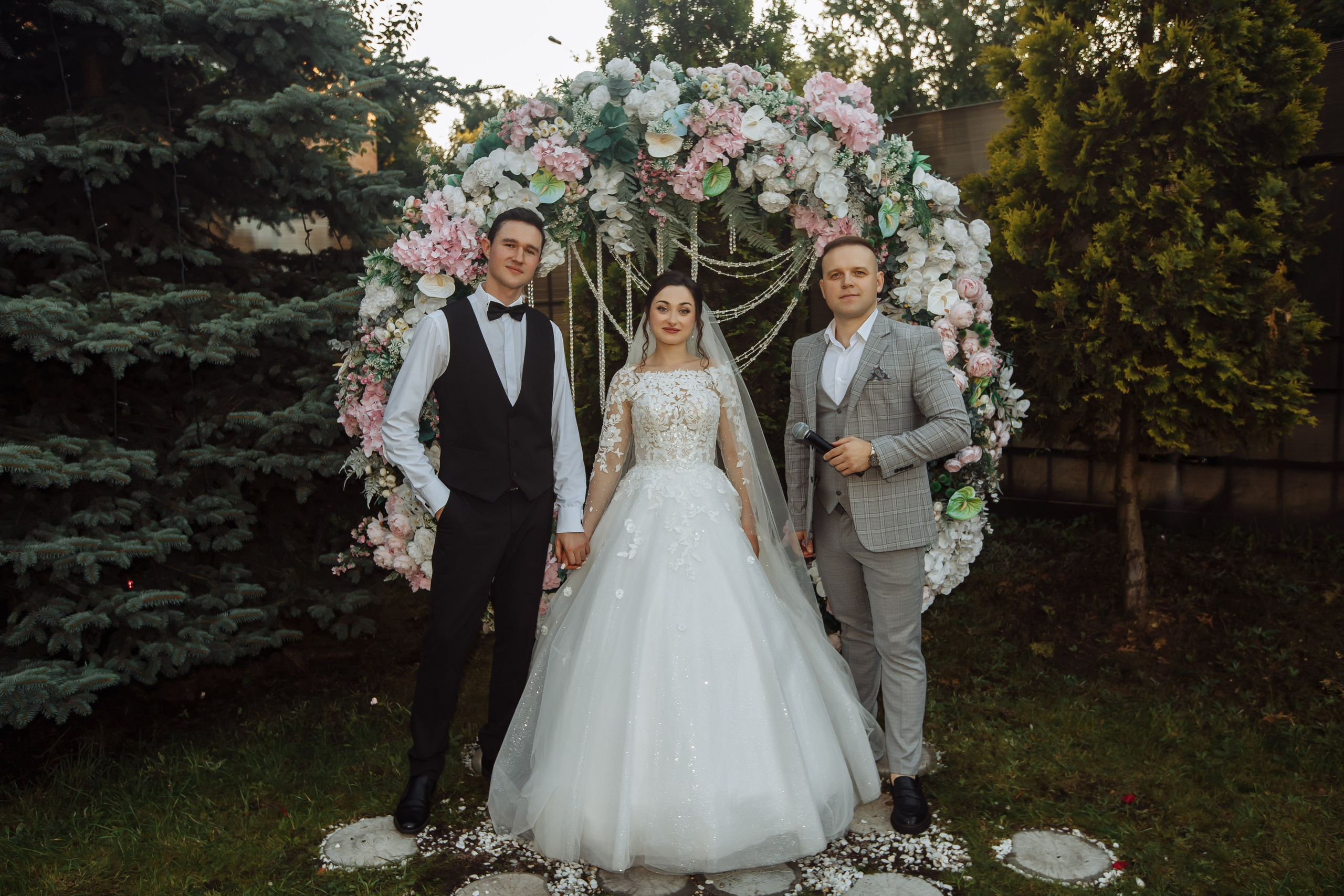 Свадебное фото жениха и невесты на фоне арки с ведущим Виталием