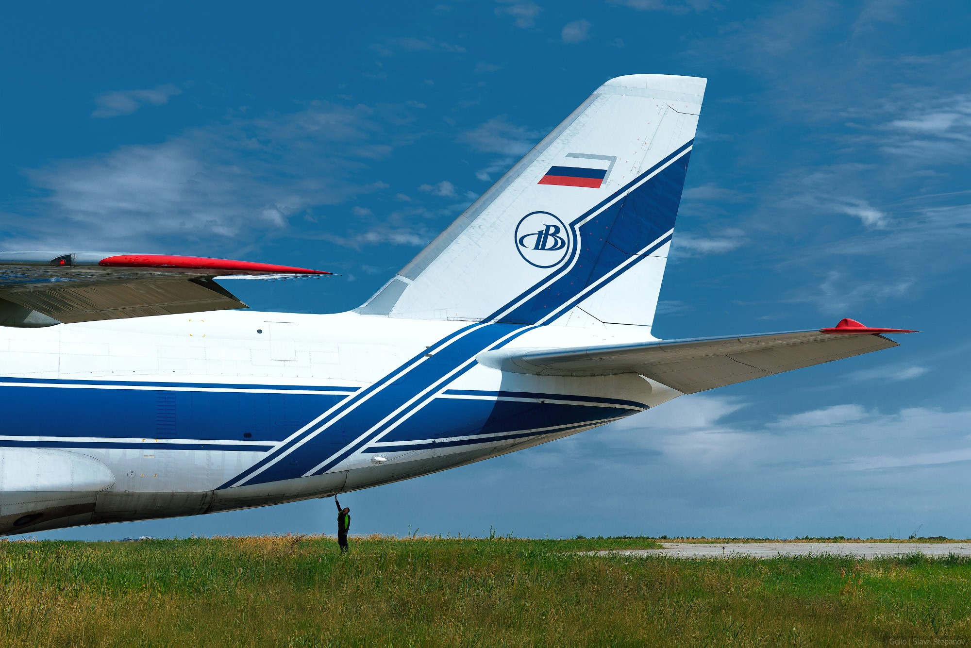 Хвостовое оперение транспортного самолета Ан-124 «Руслан» с фирменной ливреей и логотипом авиакомпании «Волга-Днепр». Человек под фюзеляжем показывает масштаб воздушного судна. Фотограф — Slava Stepanov.