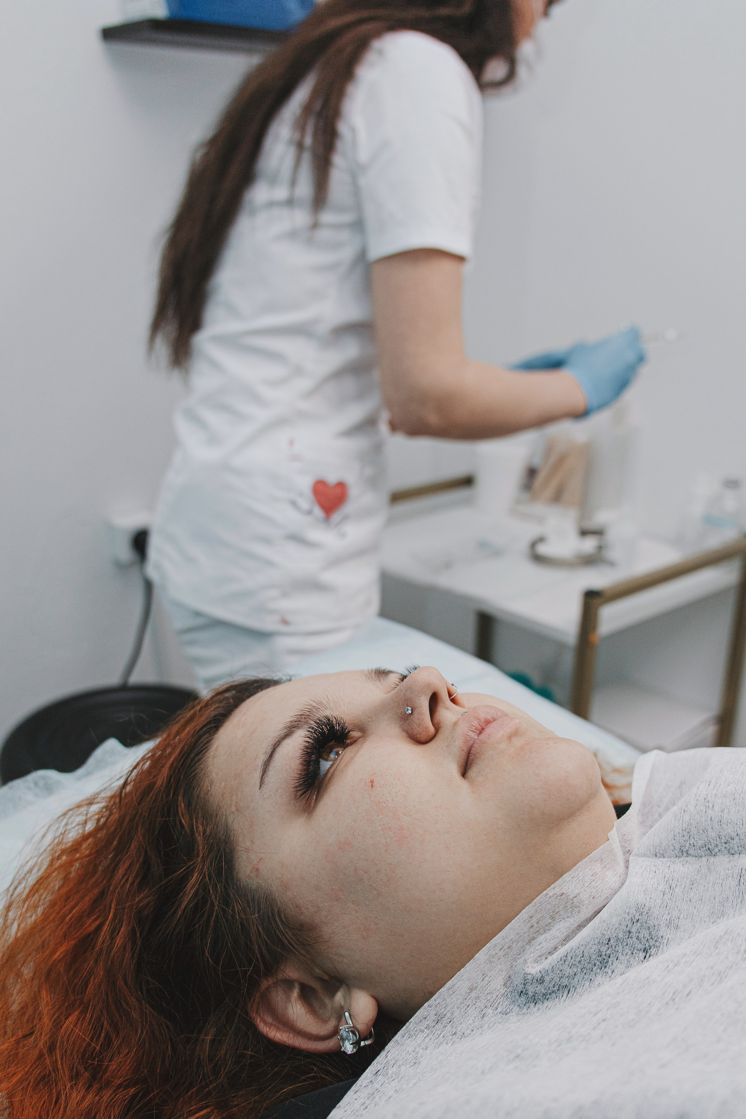 Косметолог готовится к процедуре, пациент одидает на кушетке. Стерильный светлый кабинет. Курск