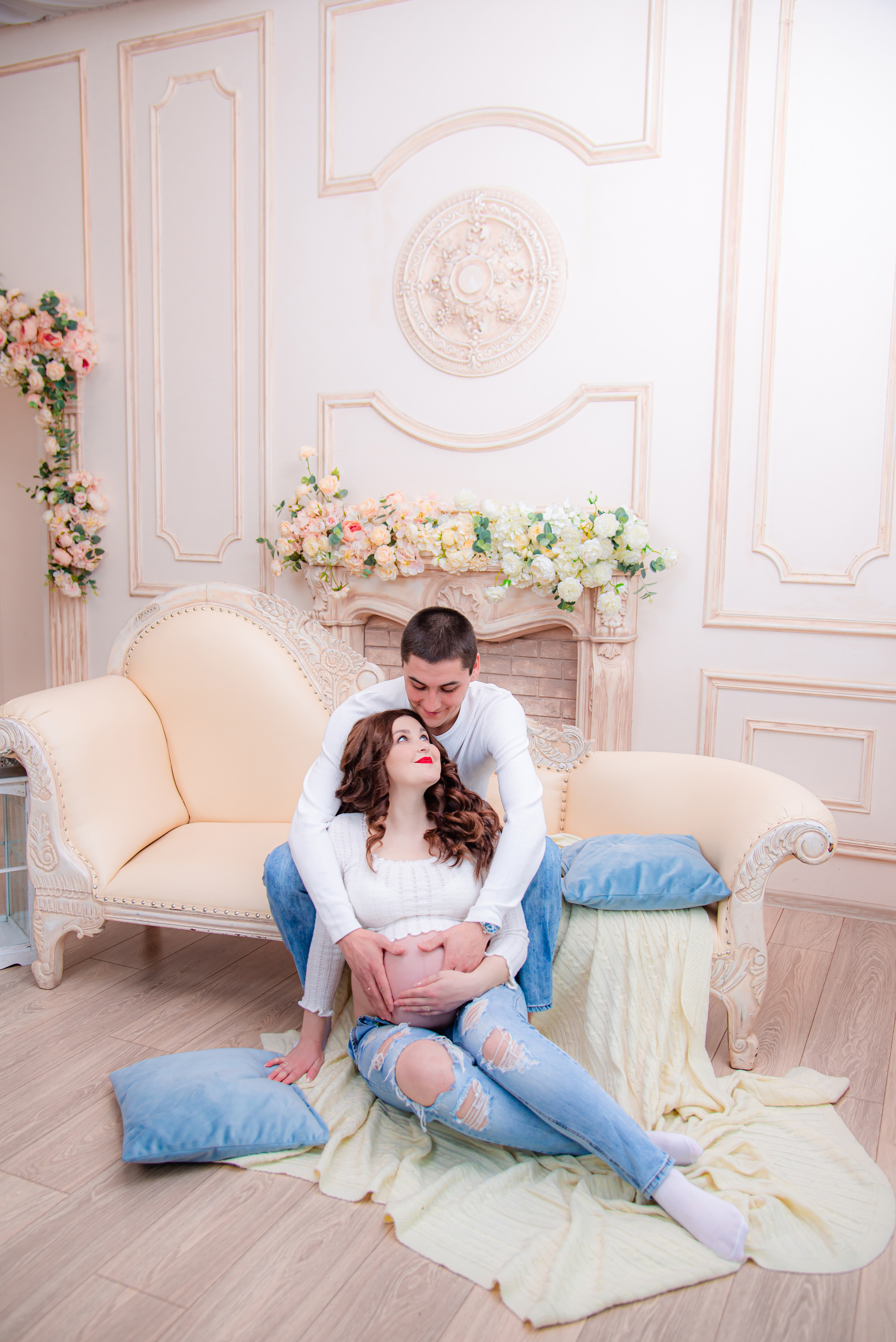 Фотосессия беременных в фотостудии в Уфе: будущая мама в элегантном платье из проката, с профессиональным макияжем и прической. Она счастливо позирует на фоне стильного интерьера, а рядом ее муж и члены семьи. Фотограф помогает в позировании, создавая теплую и уютную атмосферу, отражающую красоту и нежность материнства