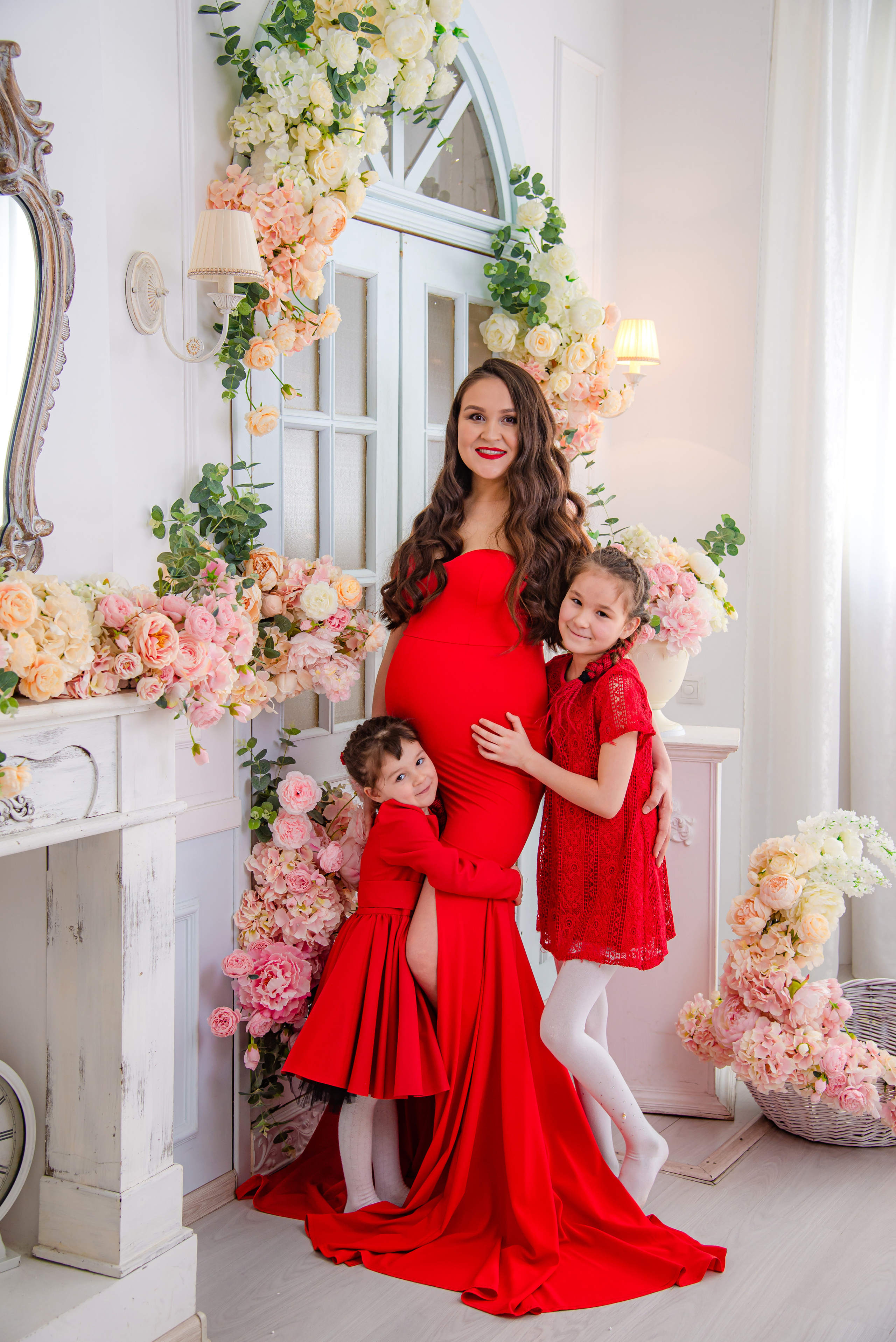 Фотосессия беременных в фотостудии в Уфе: будущая мама в элегантном платье из проката, с профессиональным макияжем и прической. Она счастливо позирует на фоне стильного интерьера, а рядом ее муж и члены семьи. Фотограф помогает в позировании, создавая теплую и уютную атмосферу, отражающую красоту и нежность материнства