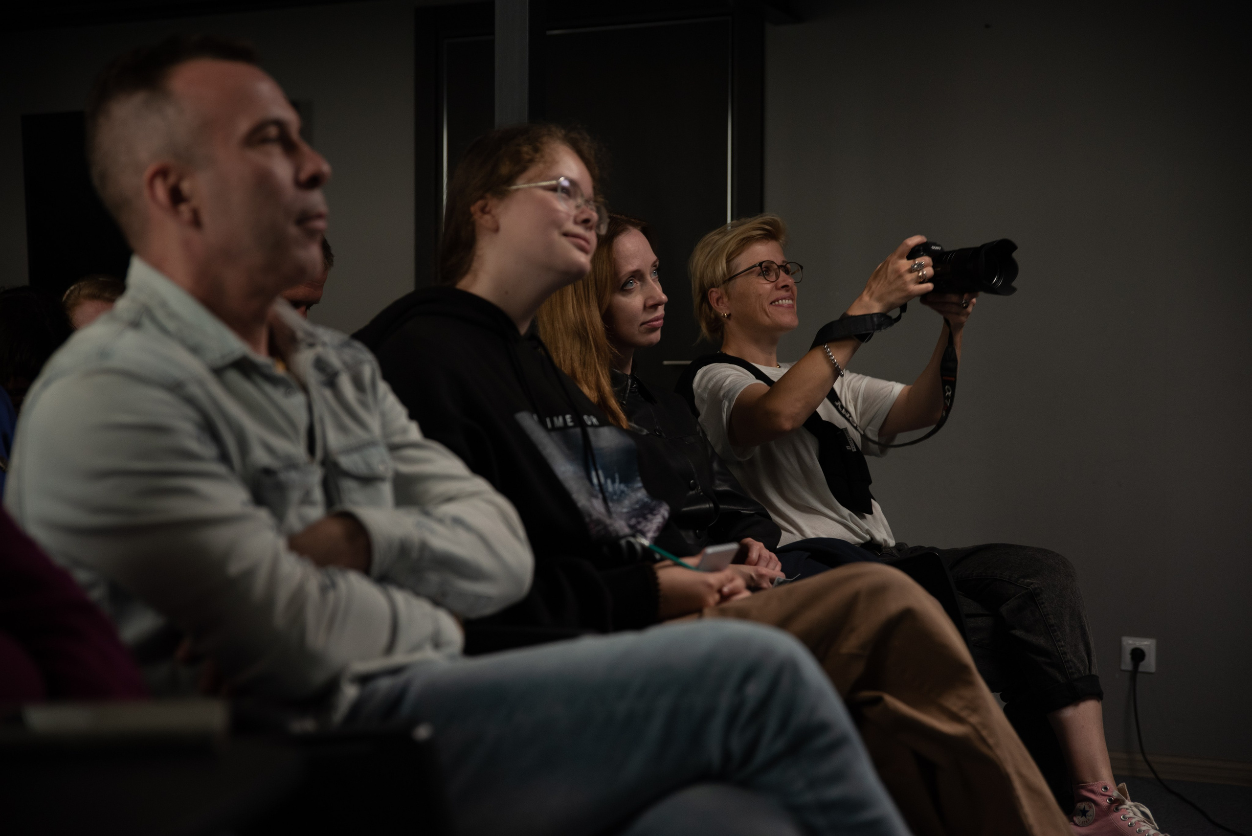 Слушатели на дне открытых дверей в фотошколе, женщина с фотоаппаратом улыбается.