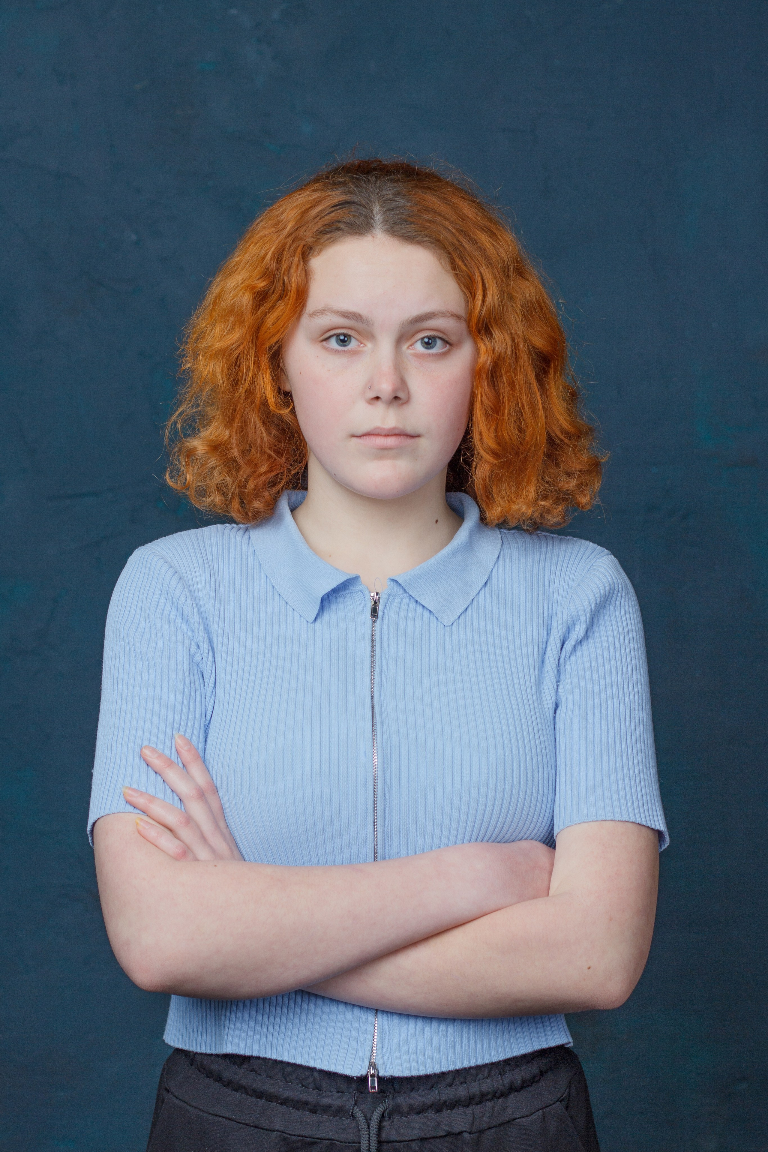 Девушка в синей блузке стоит со сложенными на груди руками