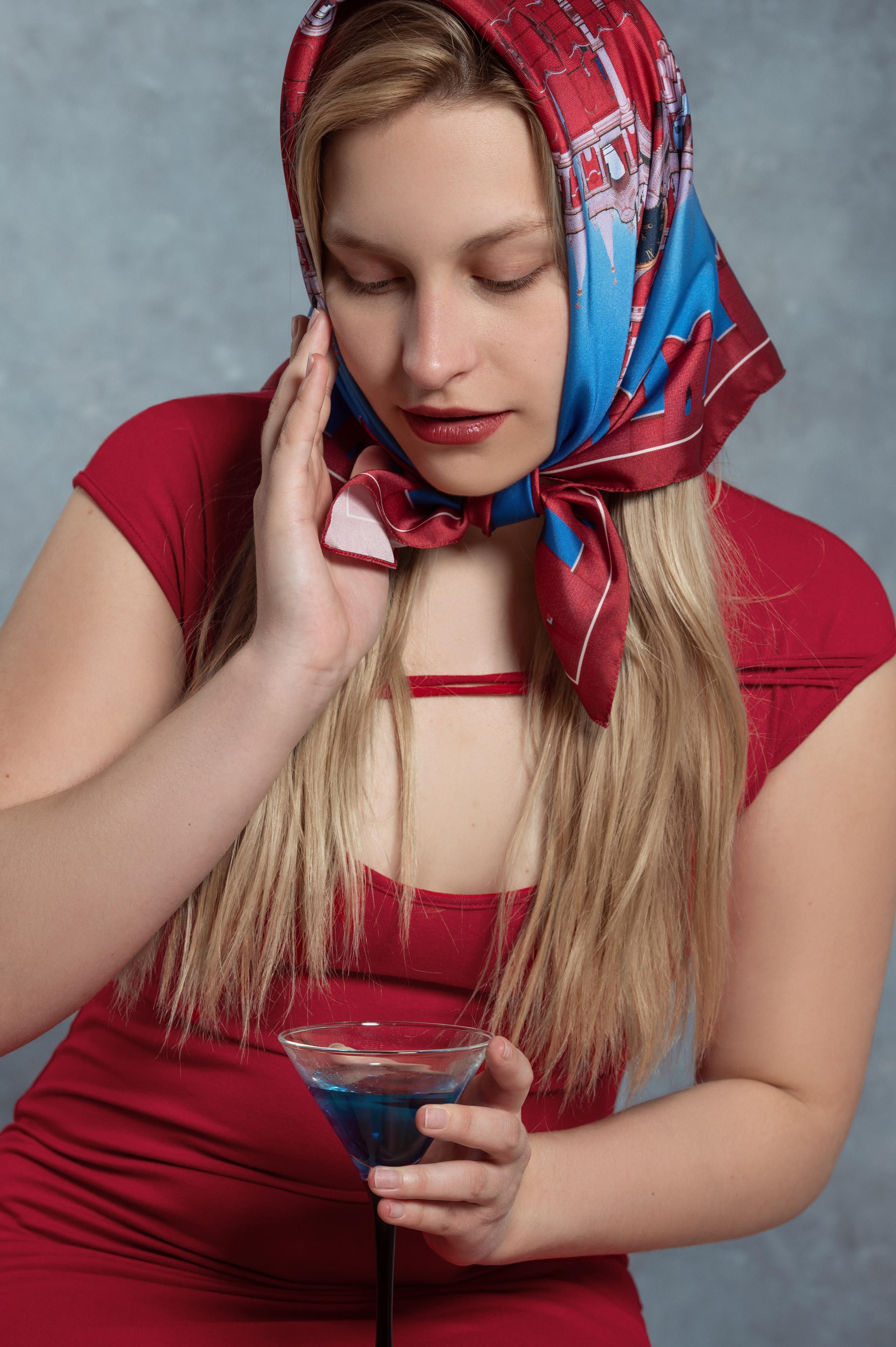 Красивая светловолосая девушка в красном платье, в платке от Serafim Cristofari "Спасская башня" и синим коктейлем в руке