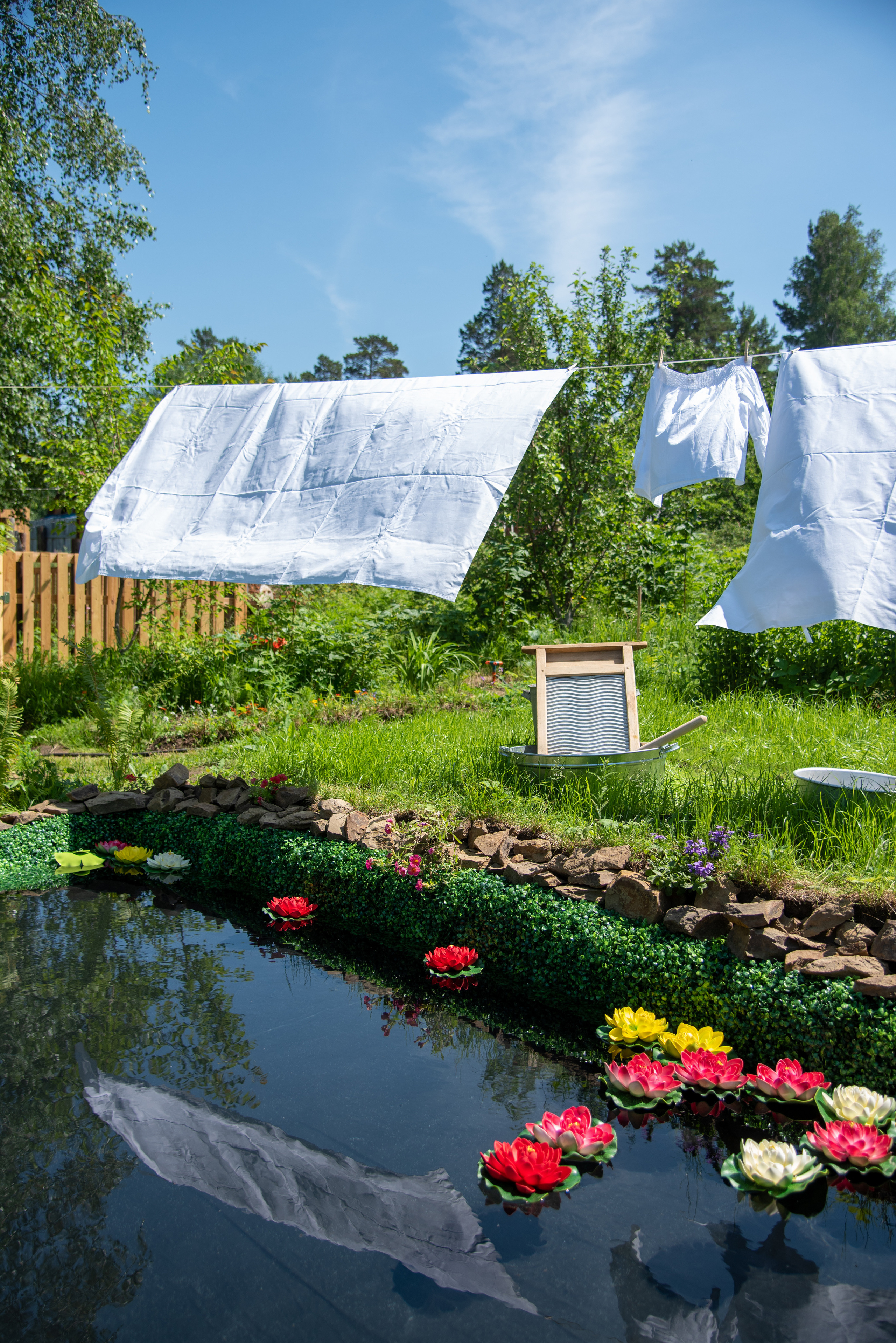 Белое белье сушится на белье вой верёвке на лужайке у пруда с лилиями