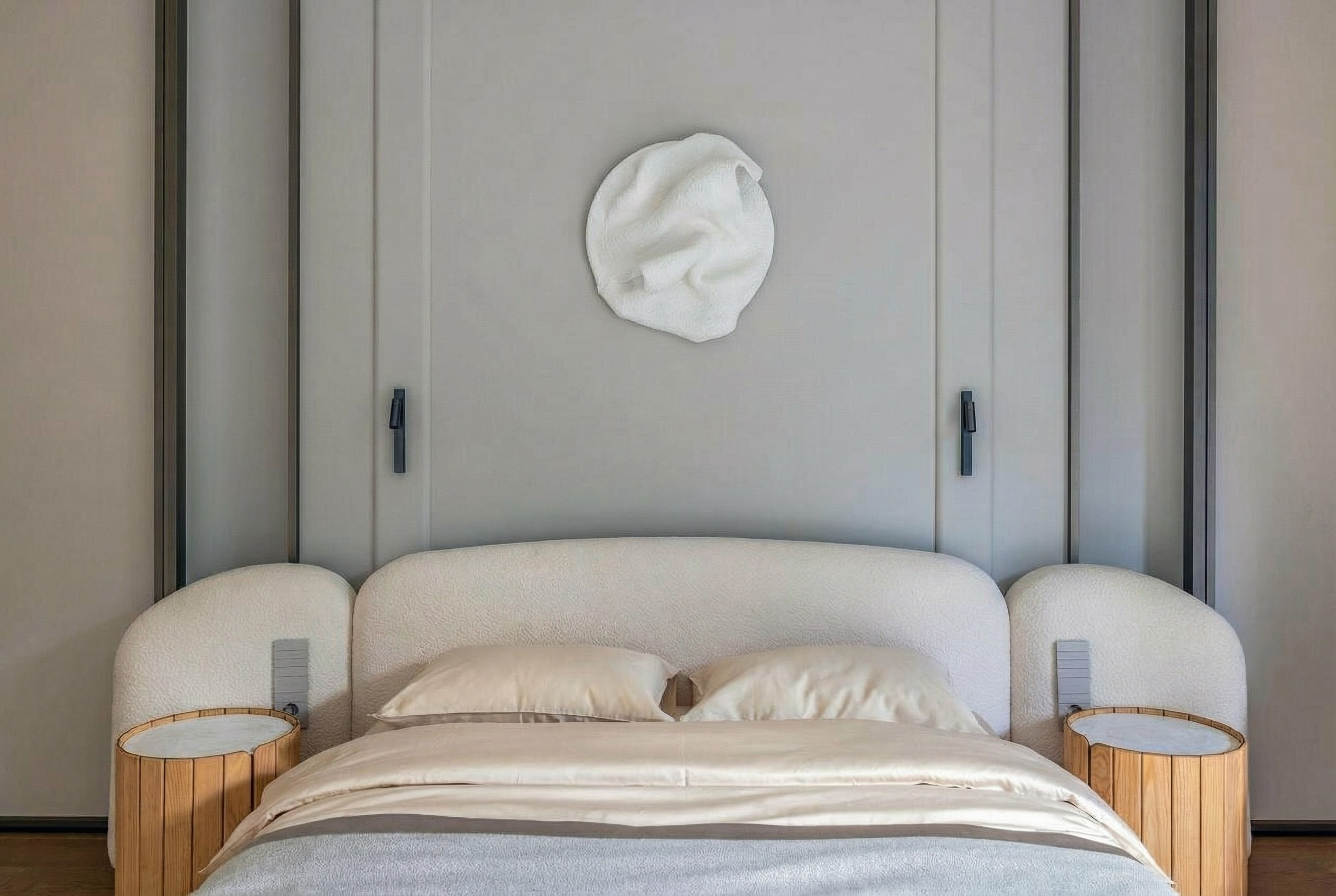 Деталь интерьера мастер-спальни: кровать с изголовьем из букле, рифленые деревянные тумбы и авторское настенное панно, проект Валерии Котович.