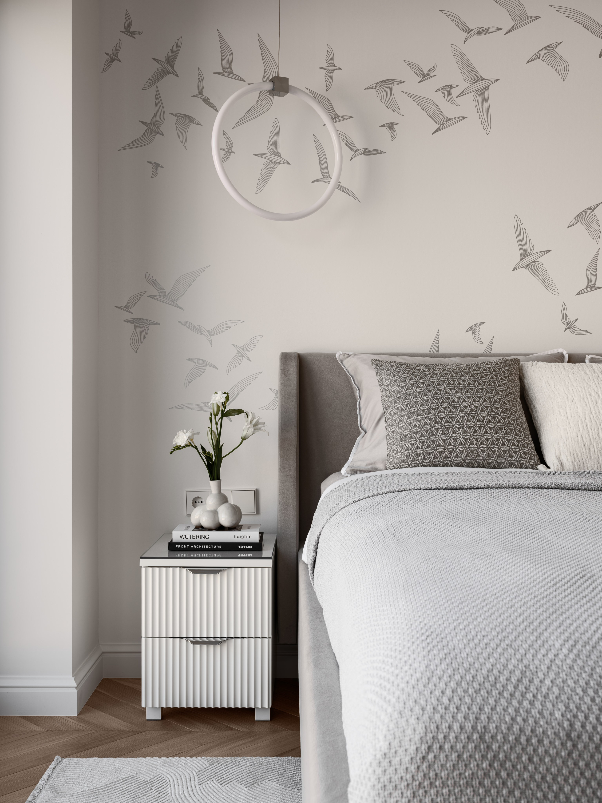 Интерьер спальни с серым изголовьем кровати, белыми подушками и настенной росписью с изображением птиц, выполненный дизайнером Алёной Боярской. Наталья Якушева подчеркнула лёгкость образа, а фотограф Сергей Денисенко запечатлел гармонию линий и светлую палитру.