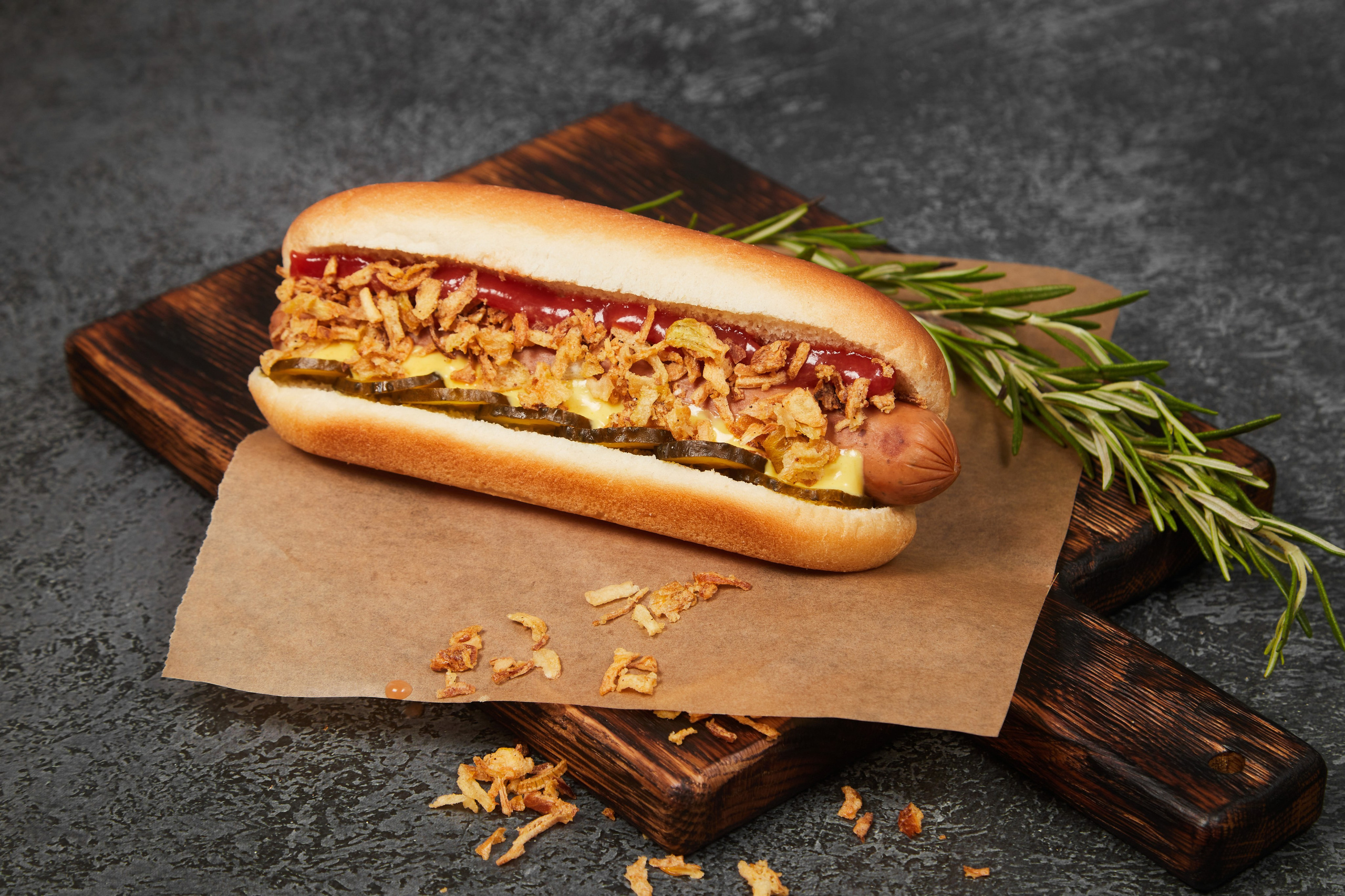 Хот-дог с колбаской и соусом на пергаменте.