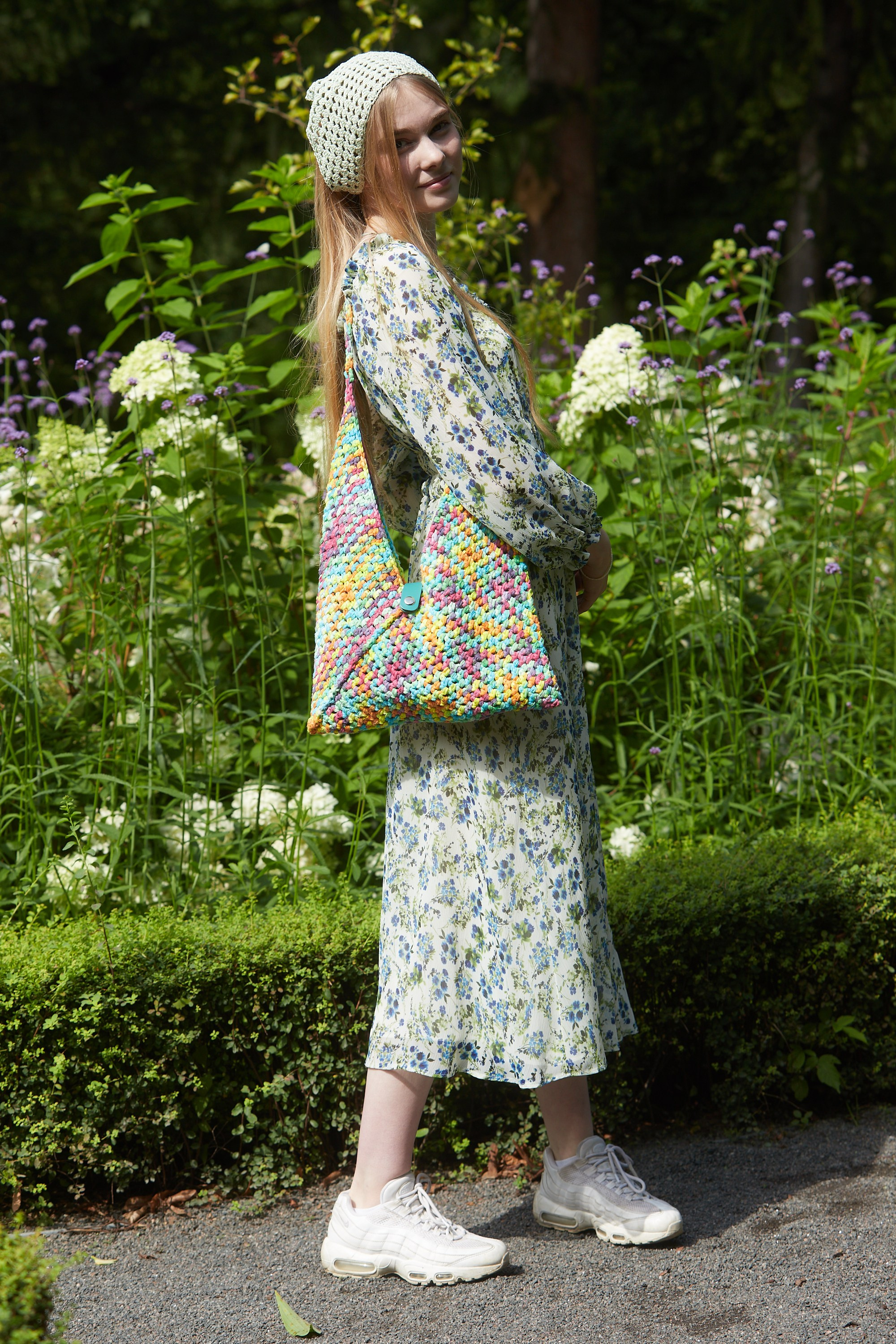 Девушка с вязаной сумкой в зелёном саду.