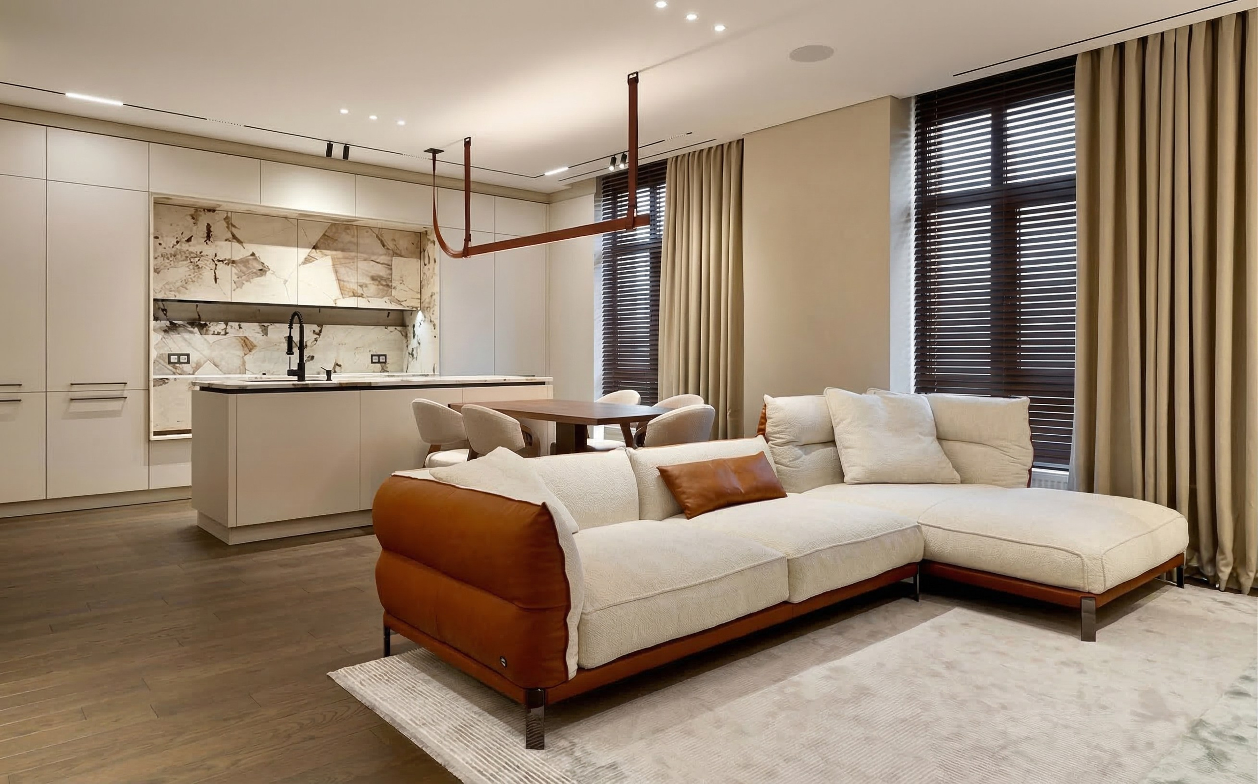 Светлая гостиная с угловым диваном в комбинированной обивке из белой ткани и рыжей кожи на фоне панорамных окон с бежевыми шторами.