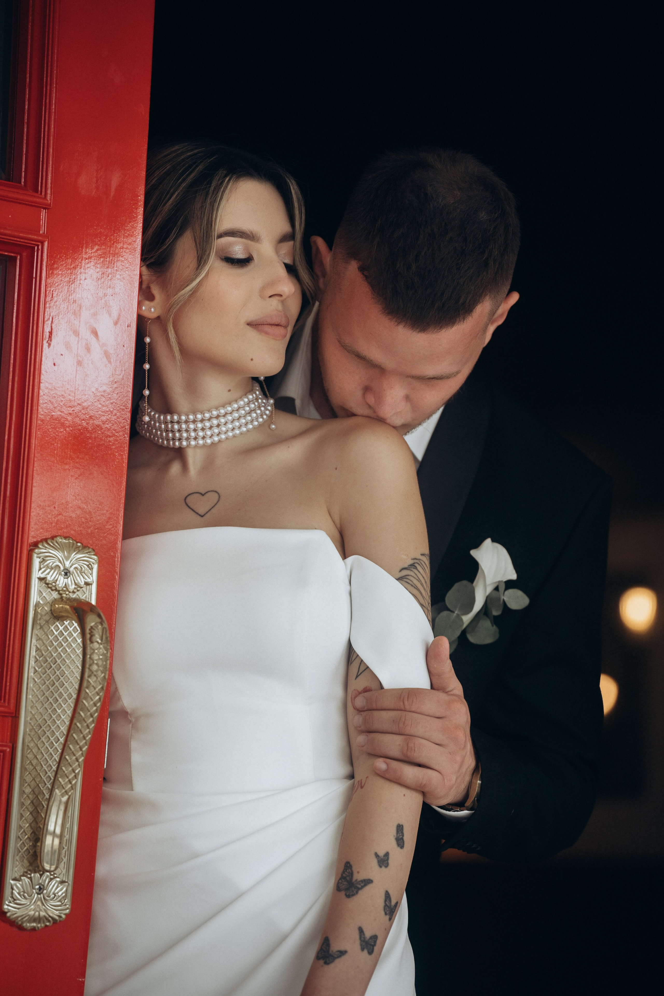 Жених целует плечо невесты, красные двери, в локациях Темрюка, в поместье Голубицкое
