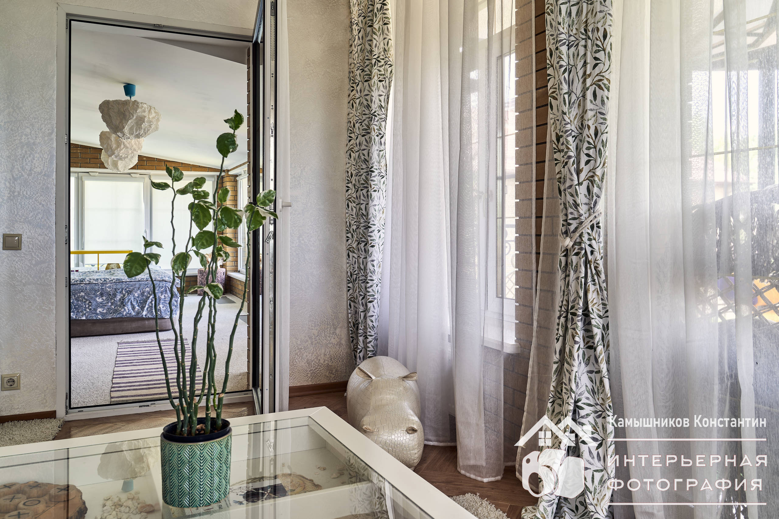 Интерьерная фотография с дверью из комнаты отдыха в большую спальню с бегемотиком, стеклянным журнальным столиком и композицией на нем