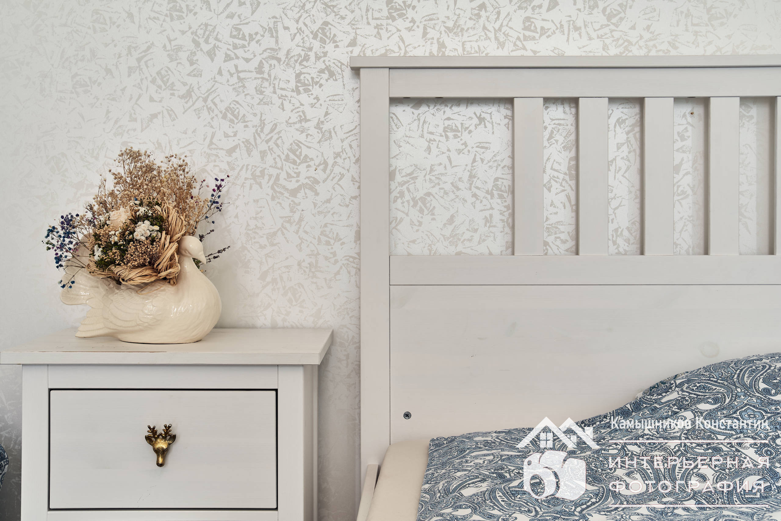 Интерьерная фотография прикроватной тумбы и части кровати в белой спальне в загородном доме в Московской области