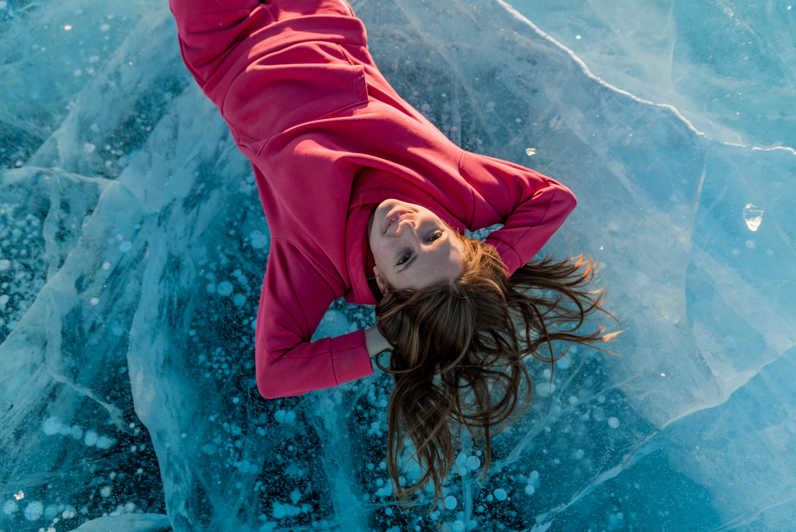 Девушка в розовом комбинезоне лежит на льду Байкала с пузырьками