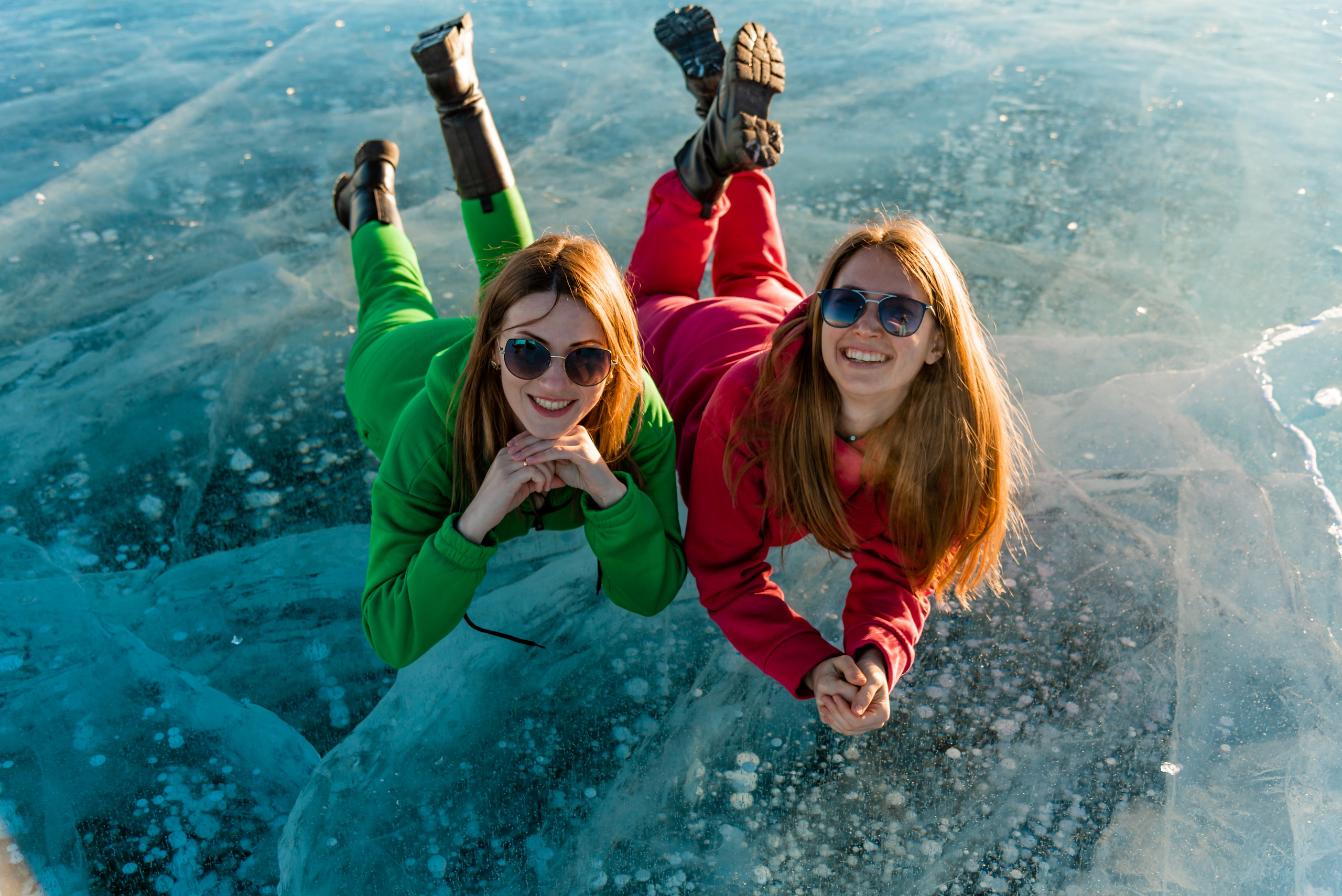 Отдых на Байкале. Цена на путевки на Байкал. Девушки в ярких комбинезонах лежат на льду Байкала с пузырьками