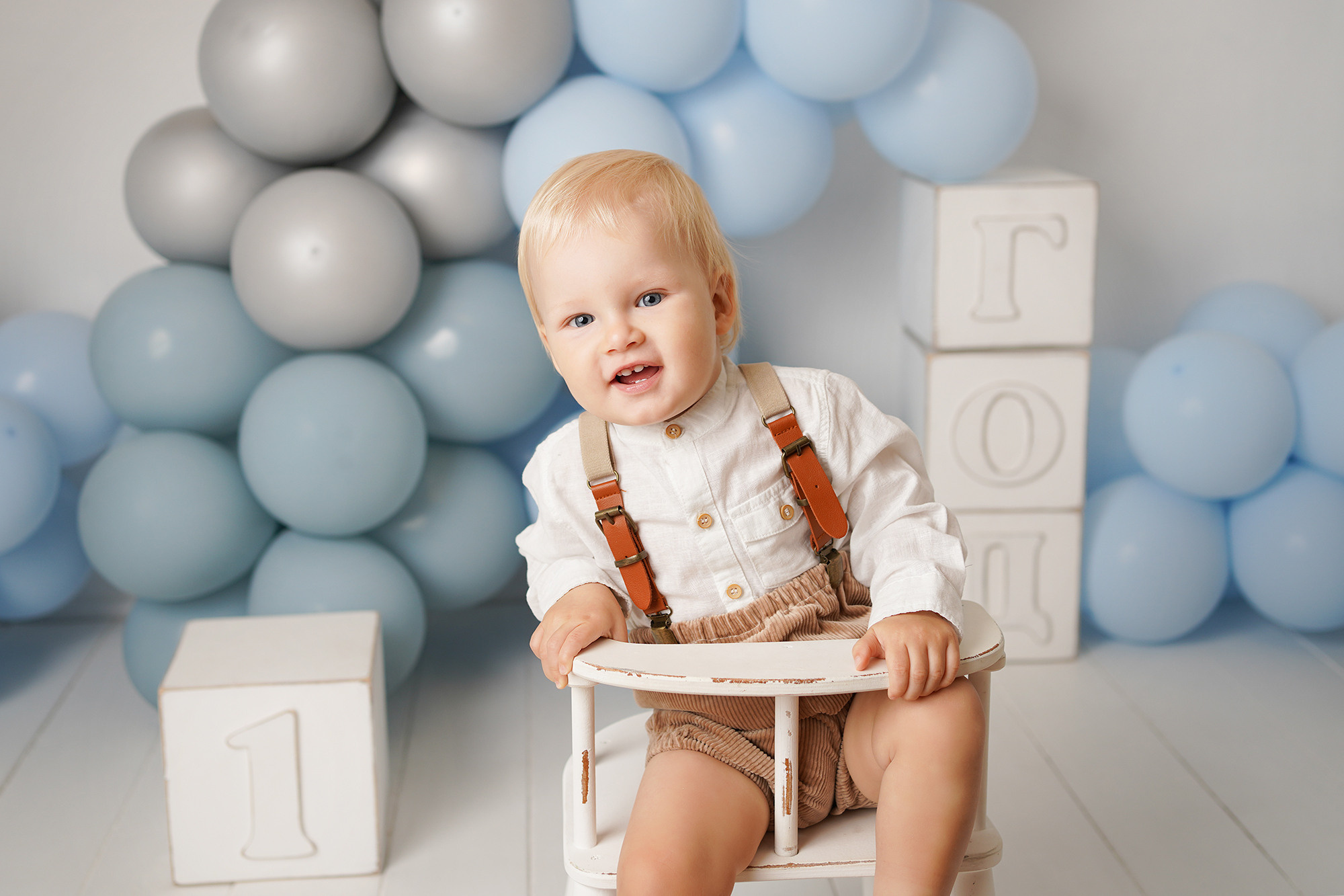 Фотограф готовит шарики, игрушки, цифру один, одежду для малыша.