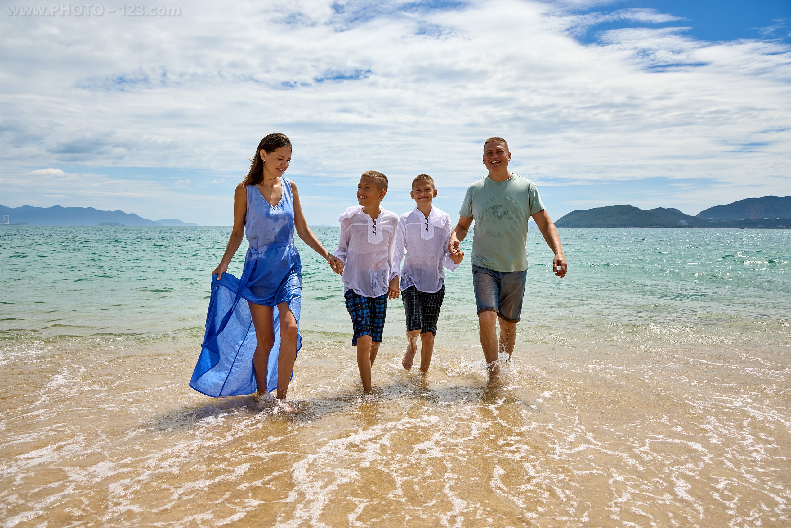 Family holding hands walking in shallow seawater along the beach | Nha Trang photographer Dima
