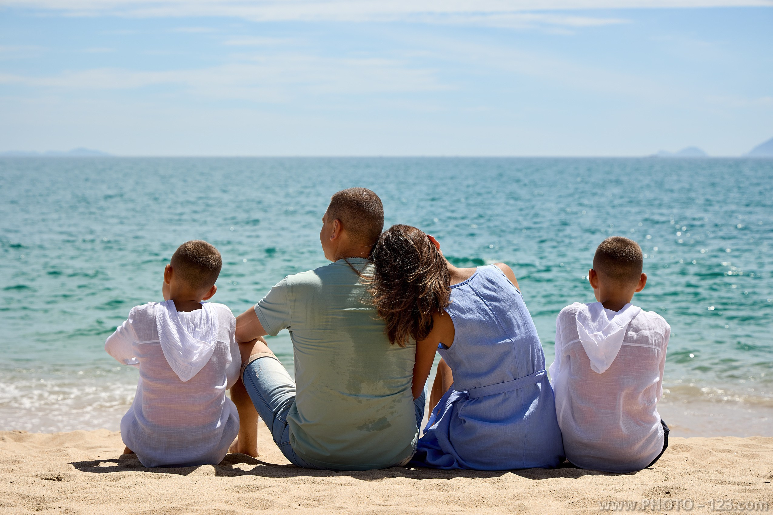 Family sitting on sandy beach with back to camera looking at the ocean | Nha Trang family photographer