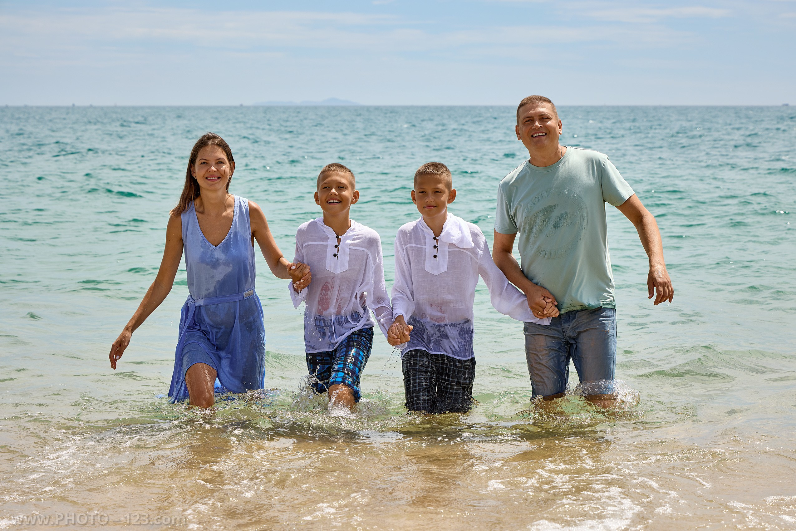 Happy family of four smiling in turquoise ocean water | High-end gear: Canon EOS R5