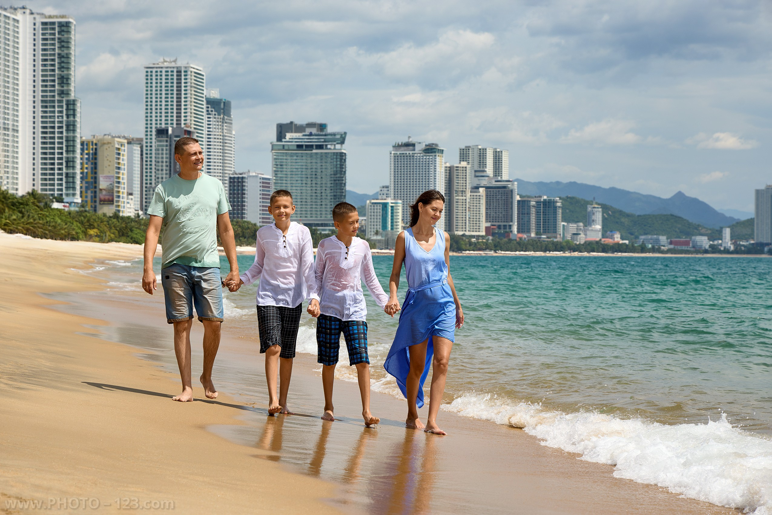 Family walking along beach shoreline with city skyline | Nha Trang family photoshoot
