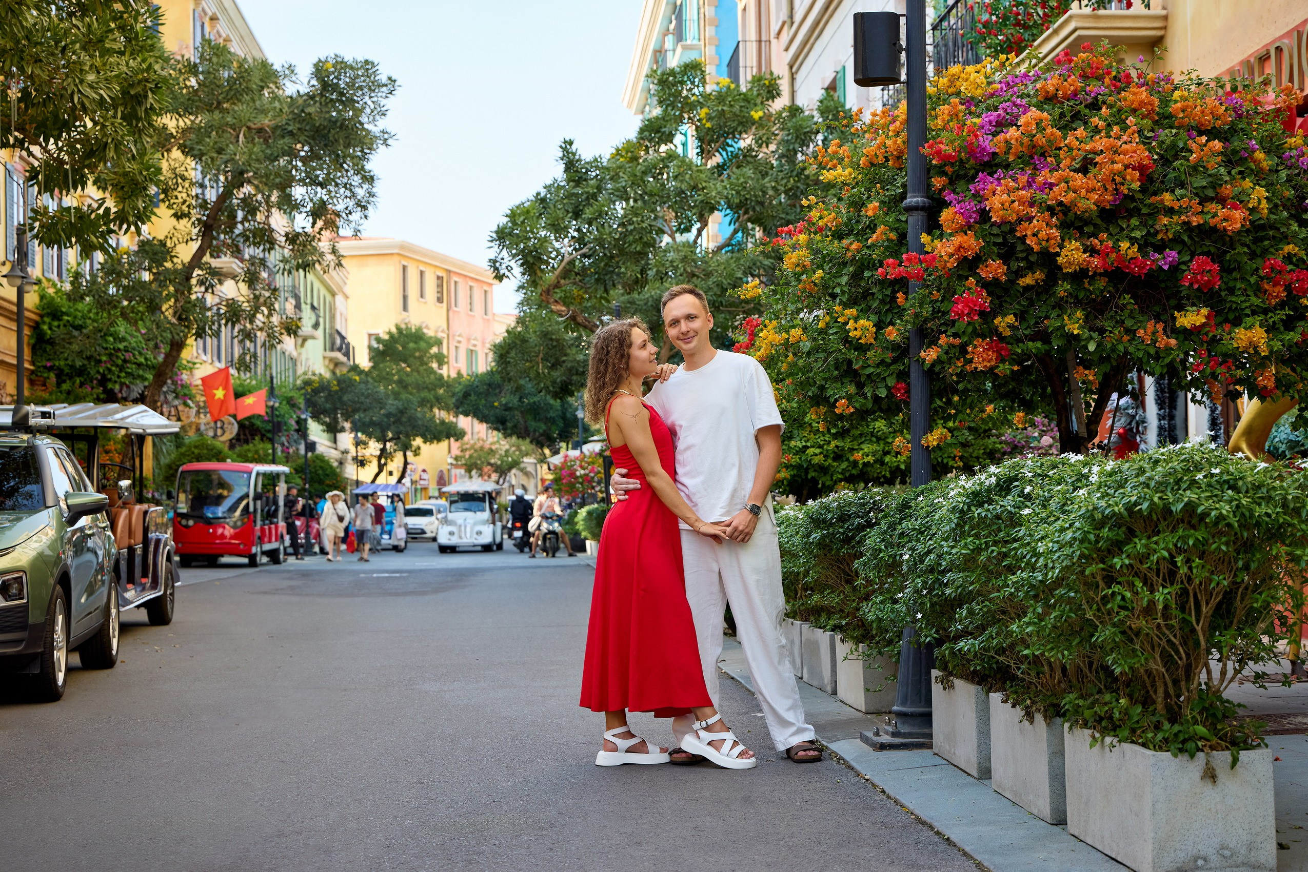 Couple strolling on a quiet, picturesque street lined with pastel buildings and flowering trees, Sunset Town, Phu Quoc, Vietnam.