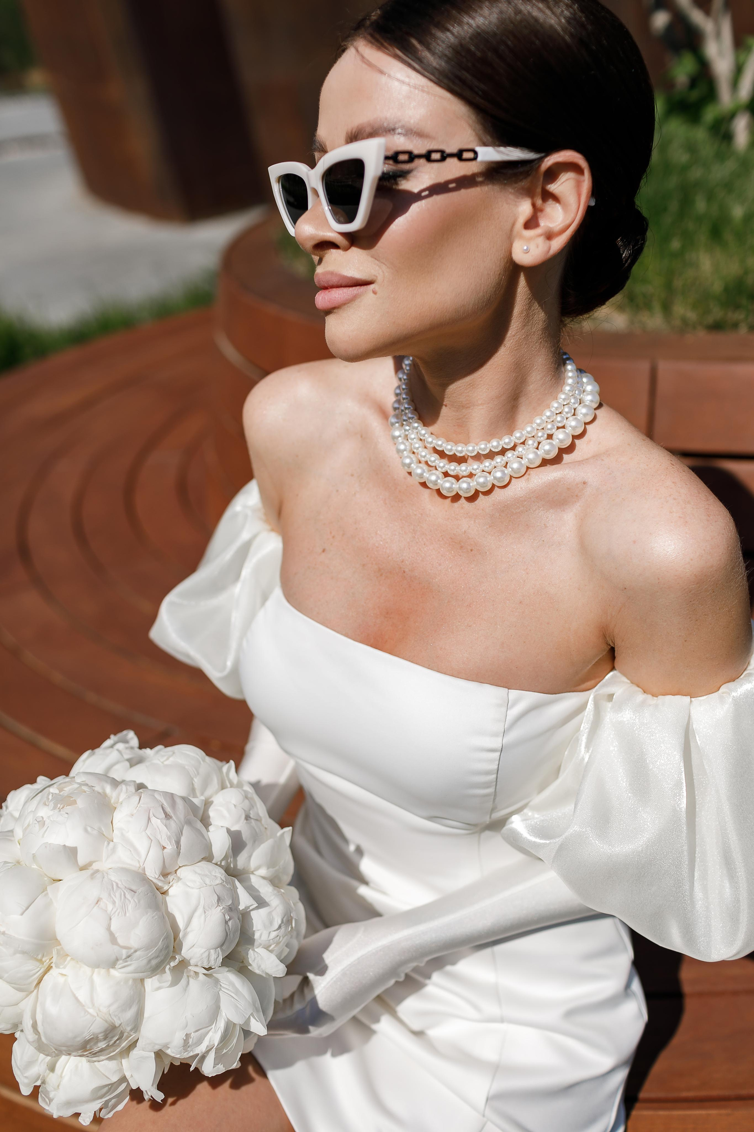 Букет из белых пионов в руках невесты в белом платье.