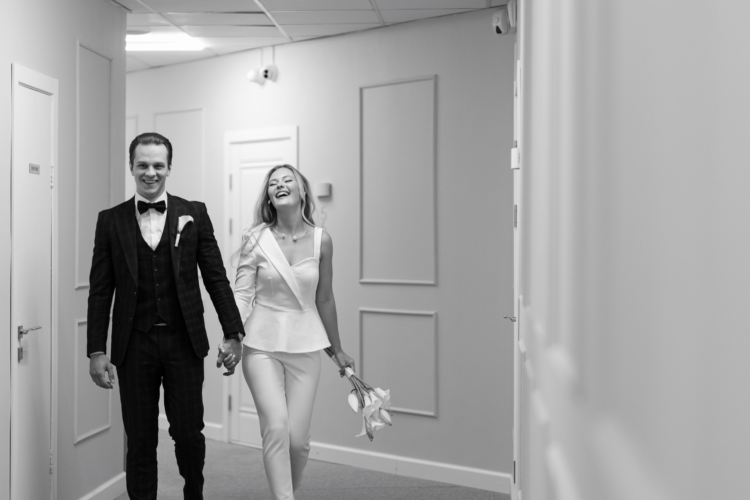 Невеста и жених идут по белому коридору , взявшись за руки.
