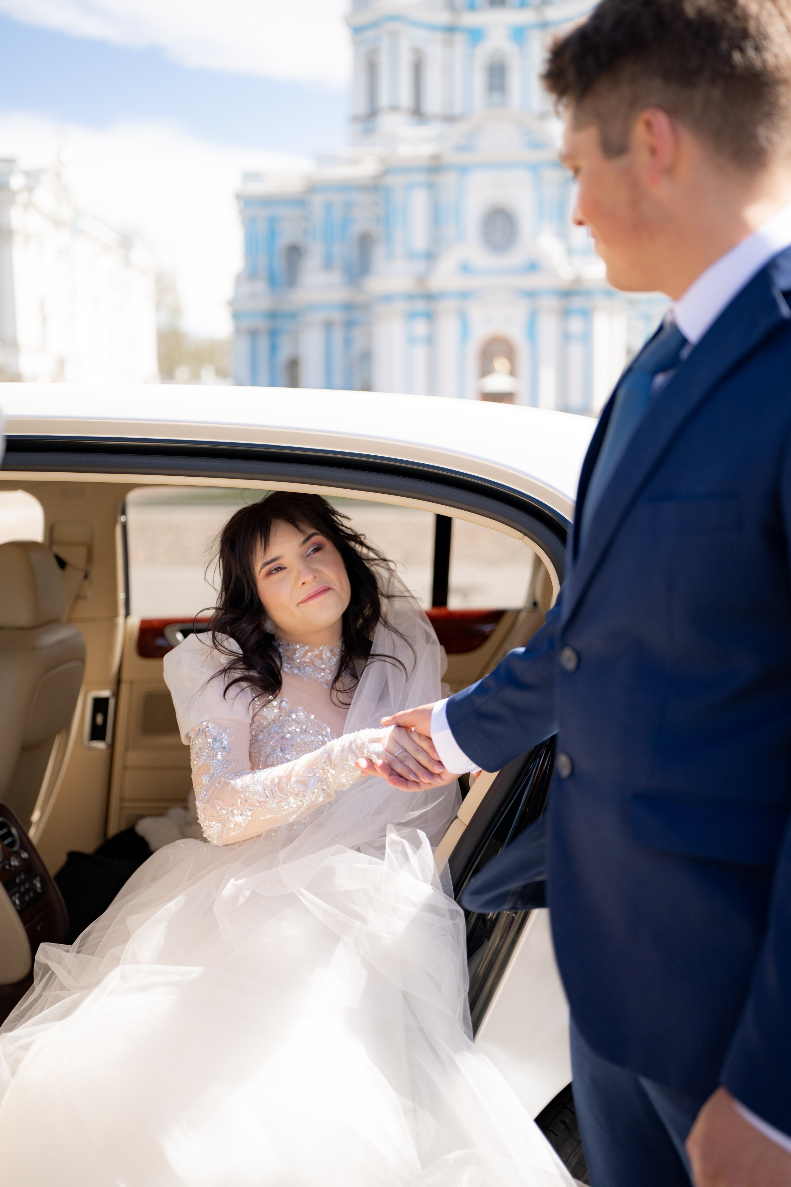Свадебная фотосессия у Смольного собора. Жених подает руку невесте руку.