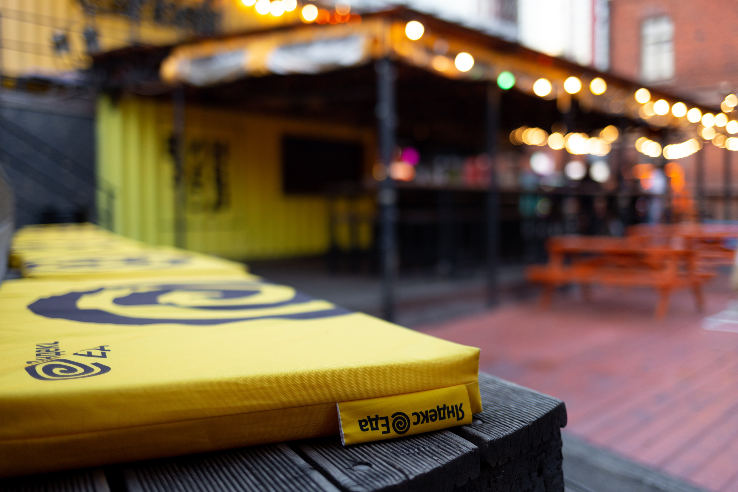 Уличная скамейка с подушками у кафе ресторана. Желтые подушки на фоне уличного ресторана.