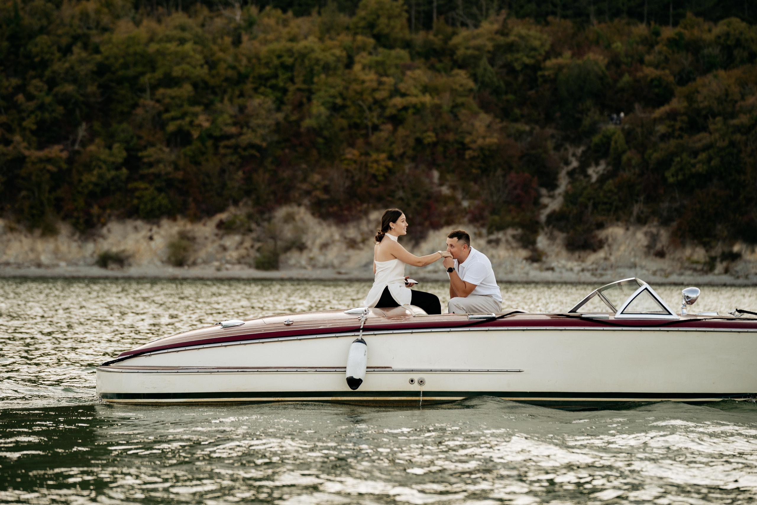 Момент предложения руки и сердца на закате. Молодой человек на одно колено на палубе ретро-катера, он протягивает обручальное кольцо. Девушка, стоя перед ним, закрывает лицо руками от счастья и удивления. На заднем плане — гладь озера Абрау-Дюрсо.