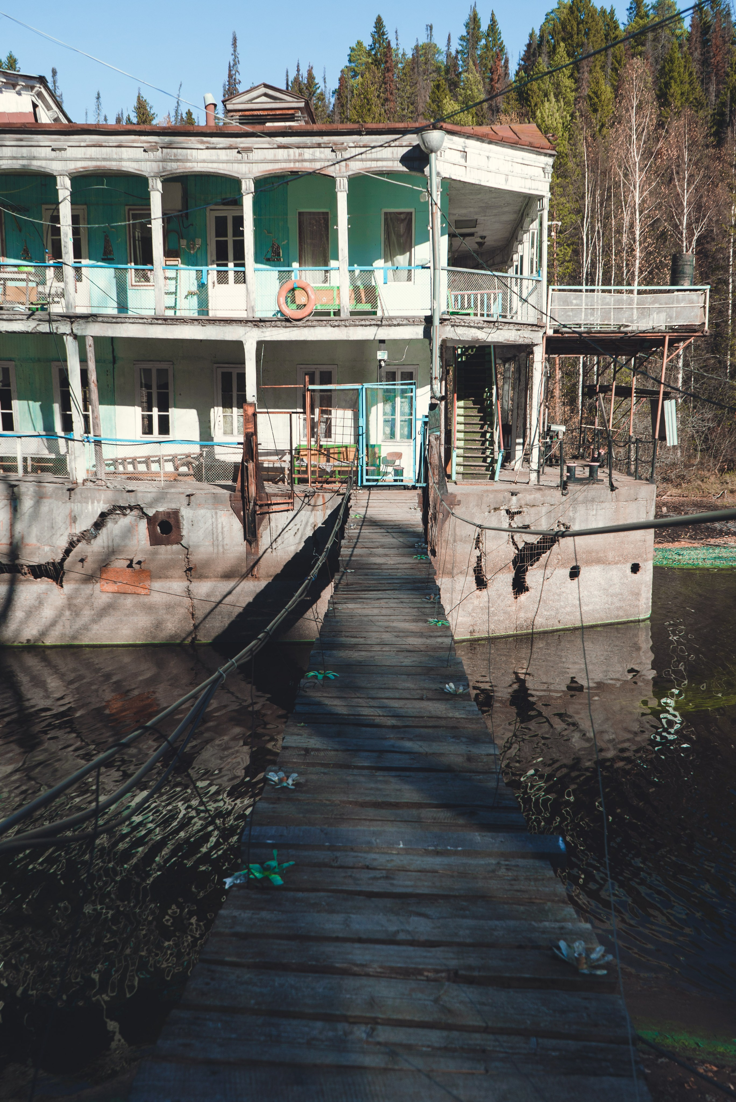 Заброшенное здание, виднеющееся на старинном берегу речной пароход, стоит на водоеме среди густого леса. Его фасад украшен колоннами и балконами, однако здание выглядит ветхим и запущенным: краска облупилась, металл покрыт ржавчиной. Вокруг голые деревья и хвойные леса, что создает ощущение уединенности и застенчивости.