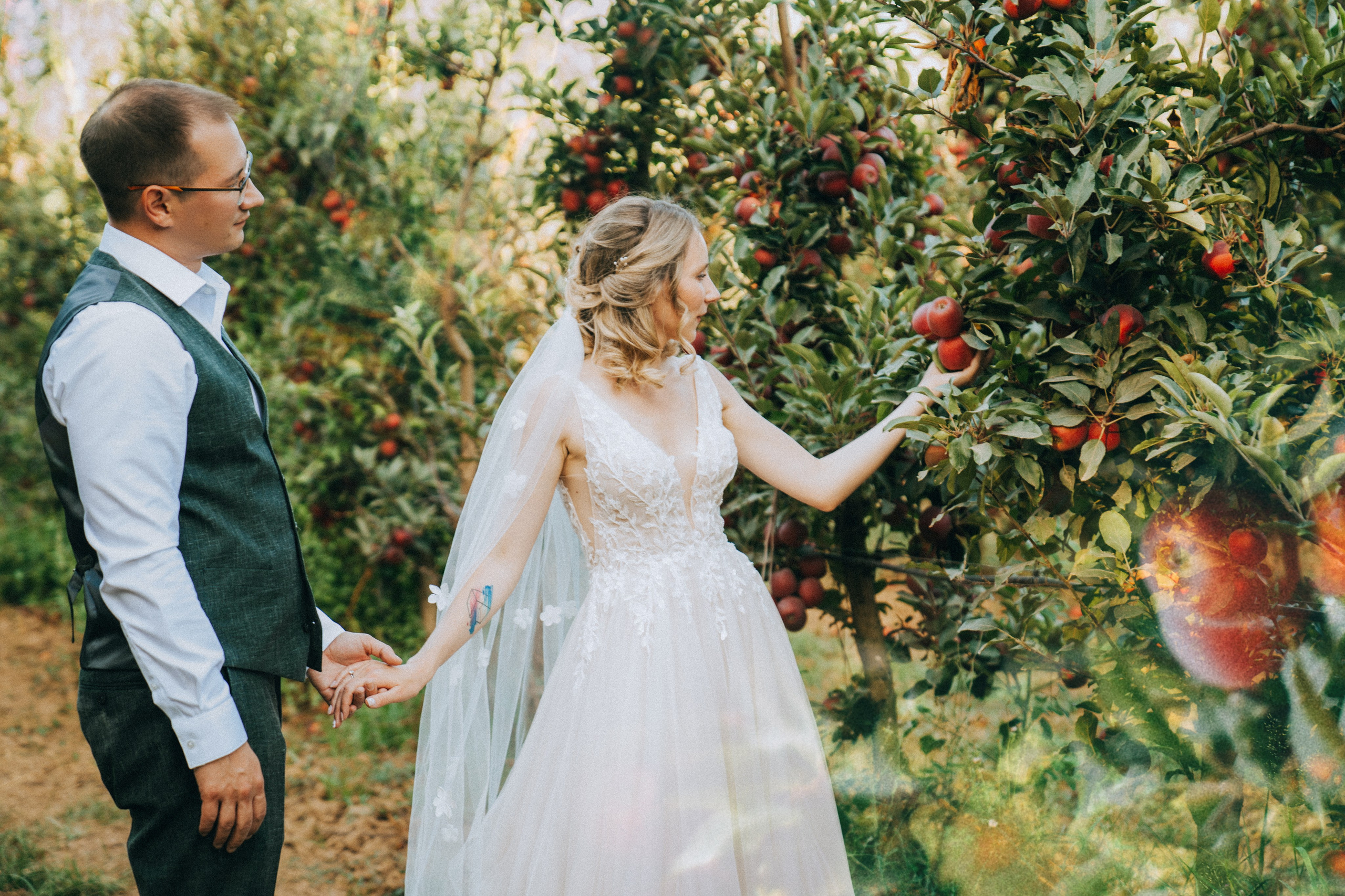 Жених и невеста обнимаются среди яблоневого сада, вокруг созревшие яблоки.