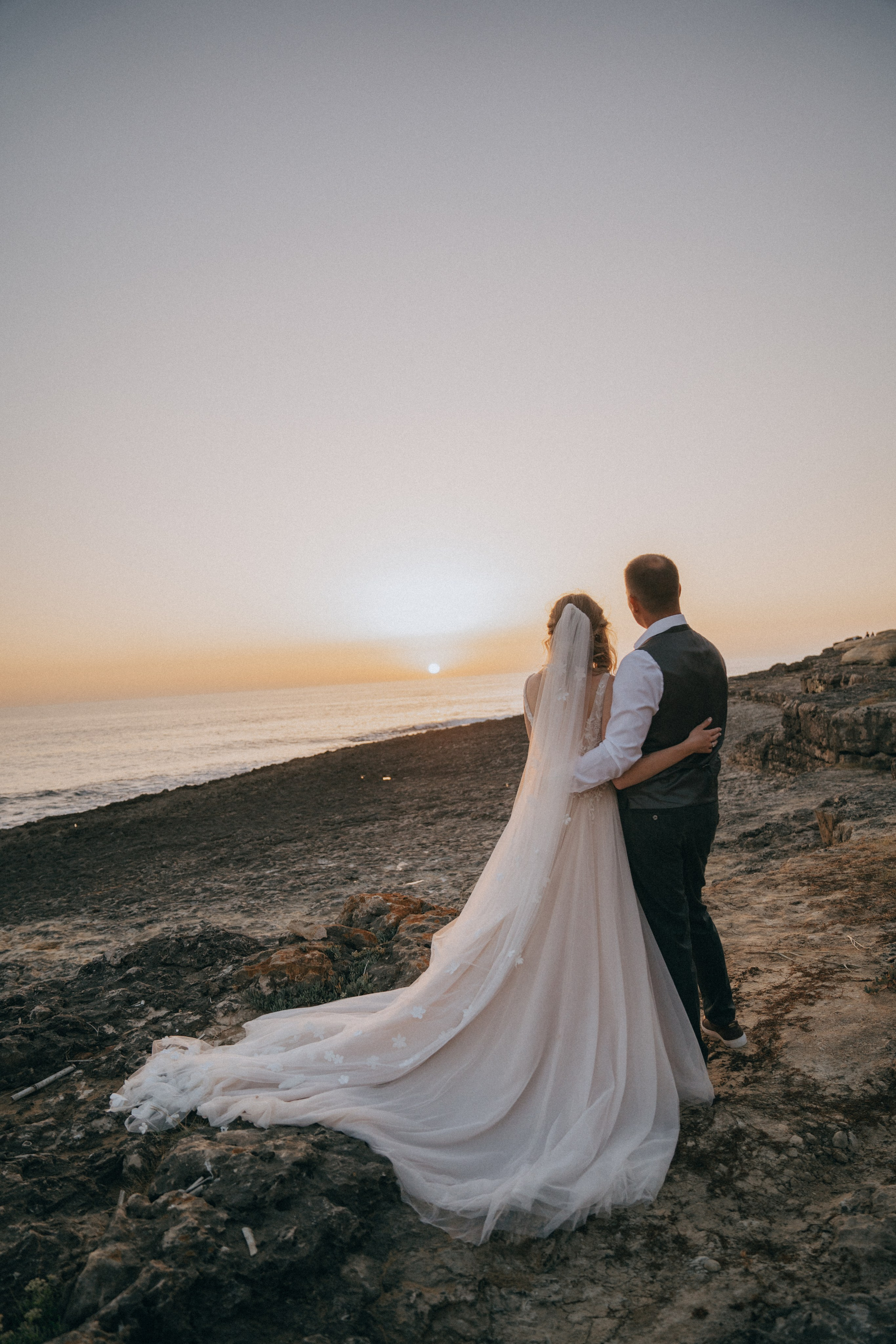 Счастливая пара жених и невеста целуется на фоне волн  скал и заката у моря океана.