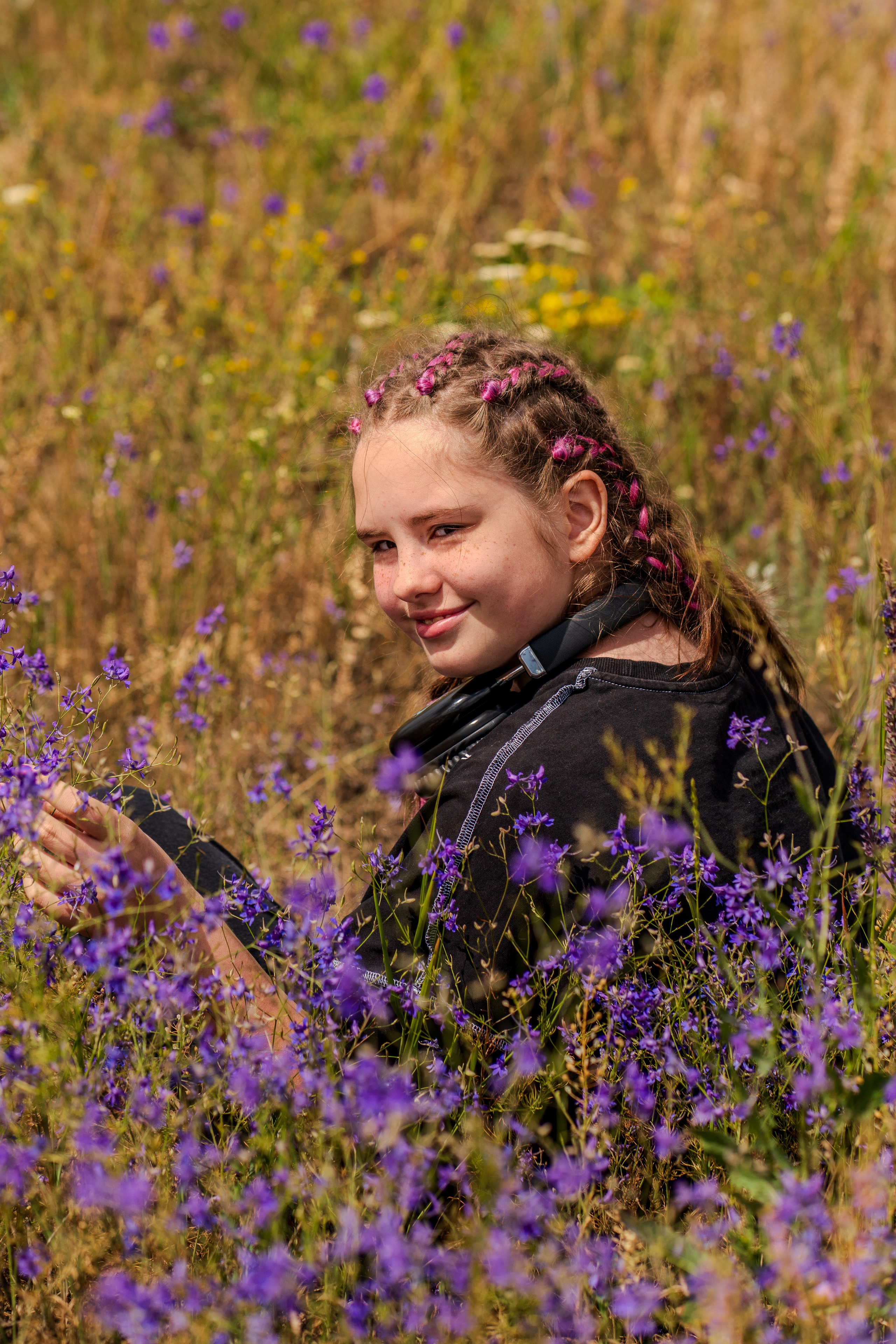 девочка сидит в цветочном поле и улыбается, фотография девочки среди фиолетовых цветов, летний отдых, фотосессия в поле, 