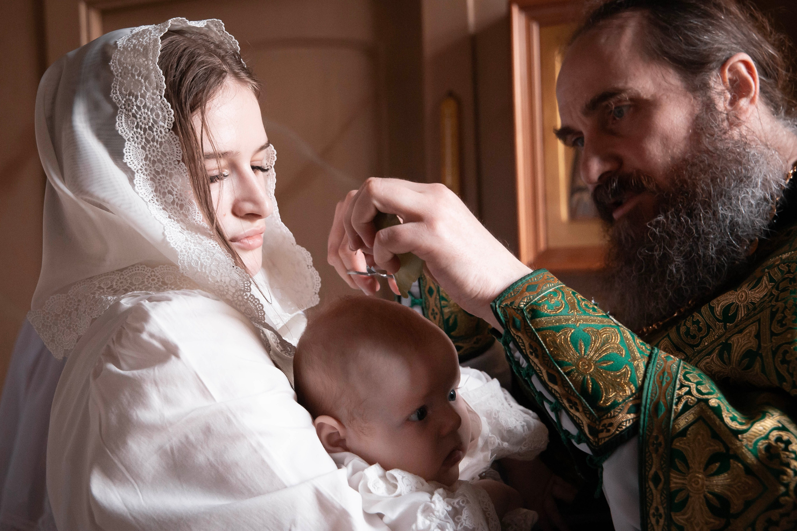 Батюшка надевает крестик во время крещения на Катюшу.