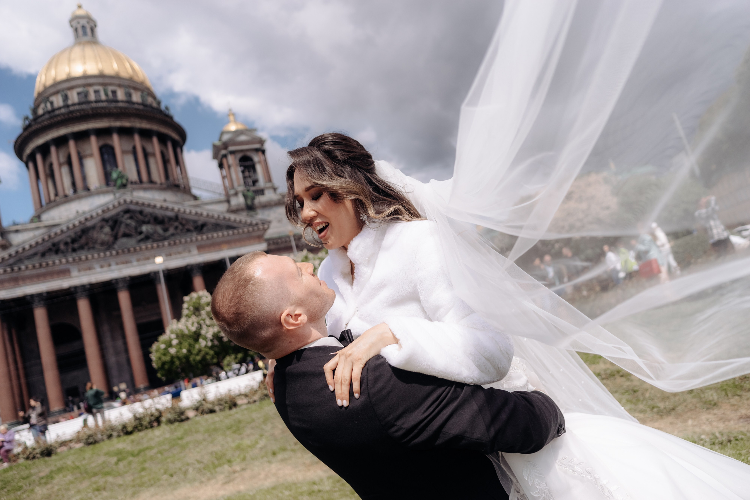 Свадебная фотосессия у Исаакиевского собора. Жених поднимает на руки невесту с развивающейся фатой на фоне Исаакиевского собора