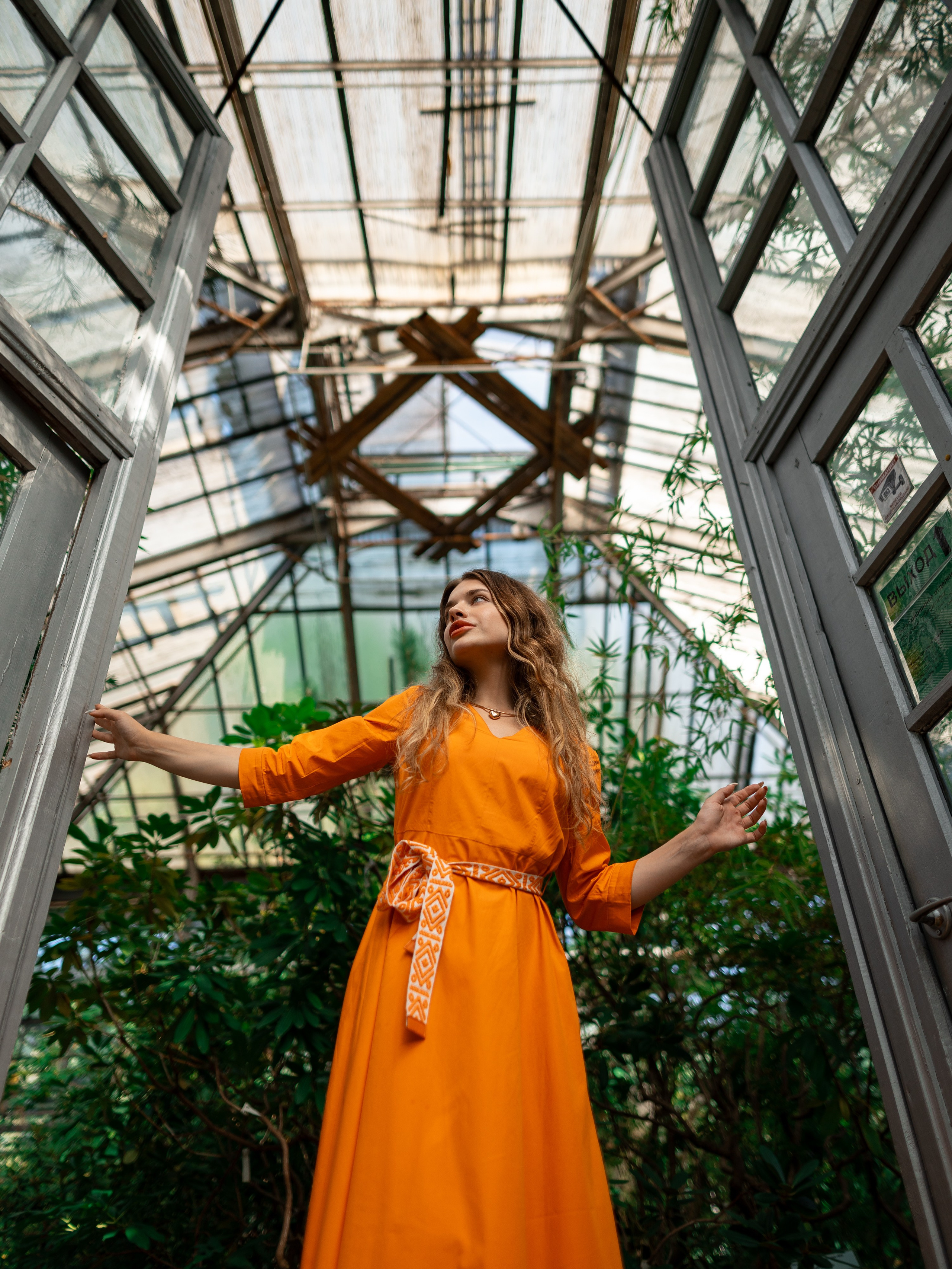 Девушка в оранжевом платье стоит на фоне зелени