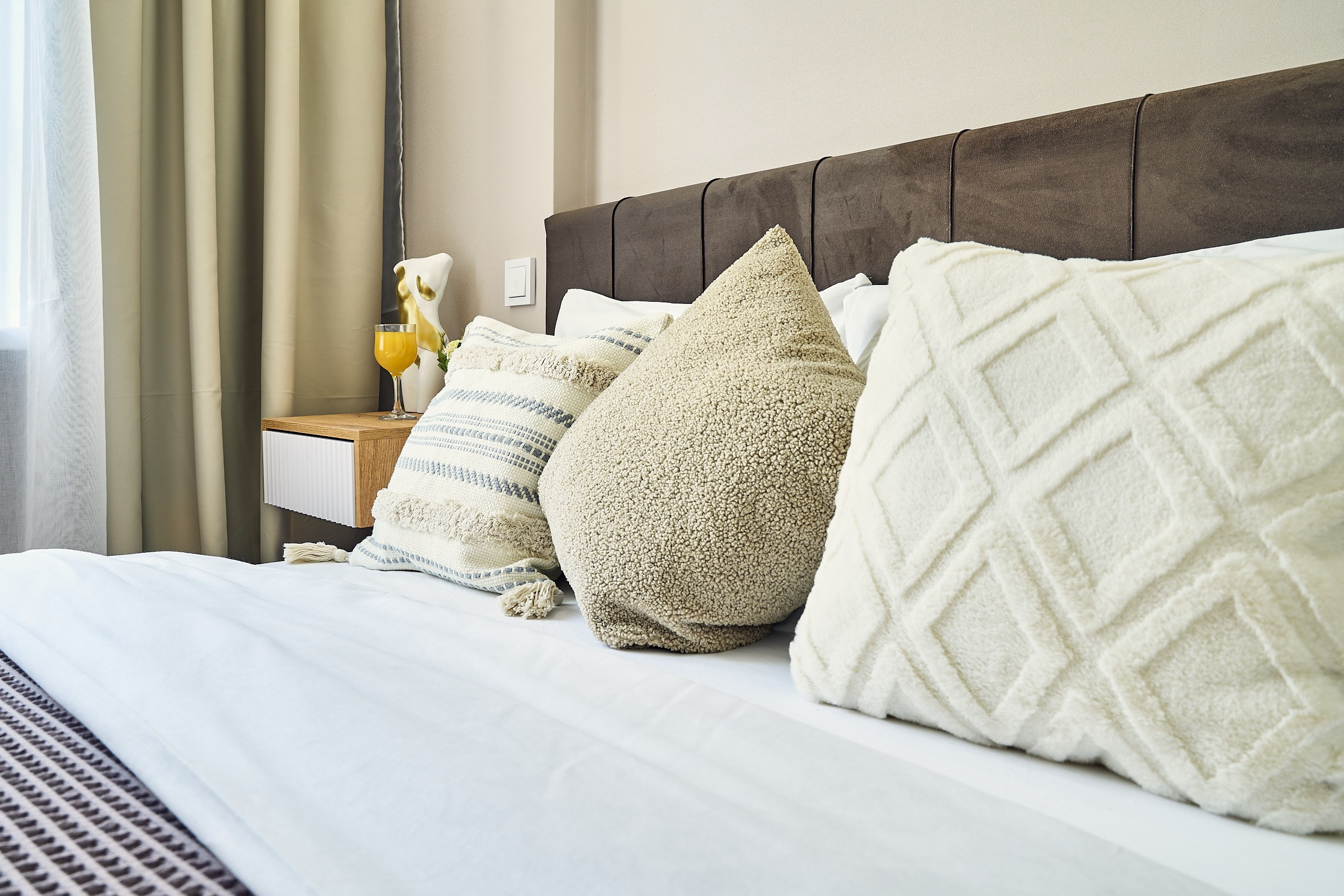 Интерьерная съемка широкой кровати с красиво расставленными подушками в апартаментах в Москве