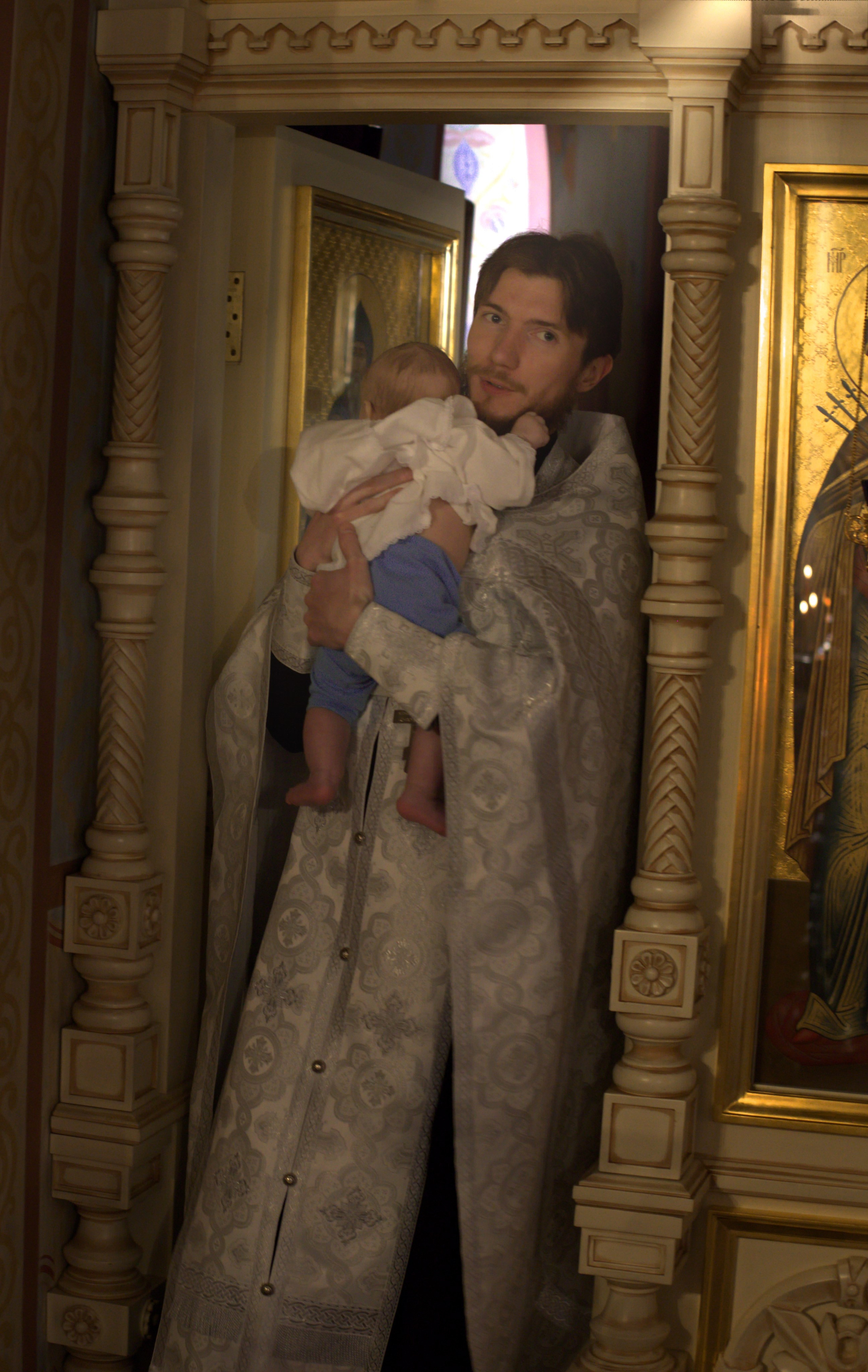 Фотосъемка крестин: священник с ребенком в церкви, обряд крещения младенца