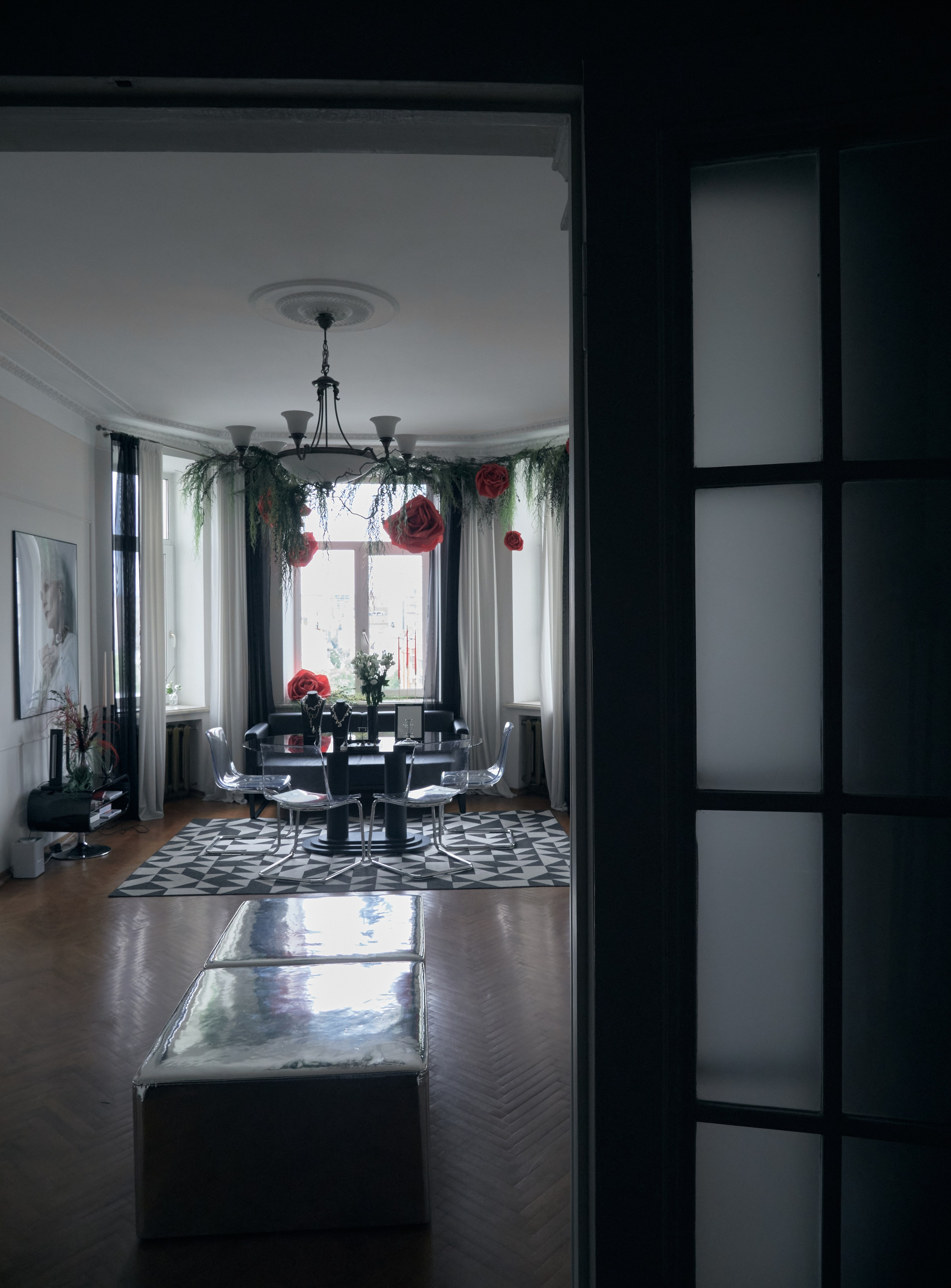 Элегантная комната с люстрой, черными стульями и праздничными гирляндами в виде красных цветов.