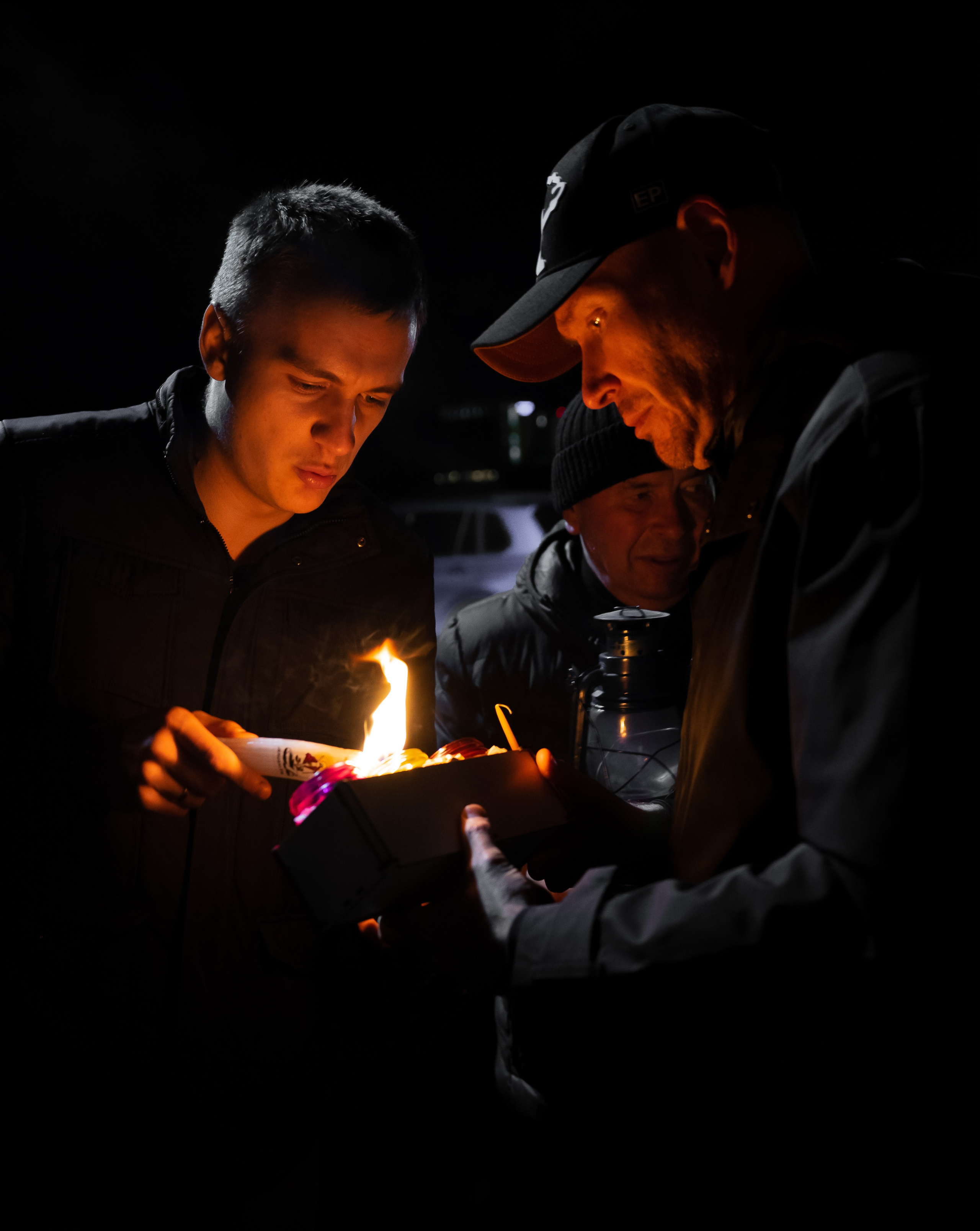 Пулково. Благодатный Огонь. Атмосферный репортаж ночного мероприятия в СПб — мужчины зажигают свечу от лампады, эмоциональный кадр фотографа Евгения Мальцева. 