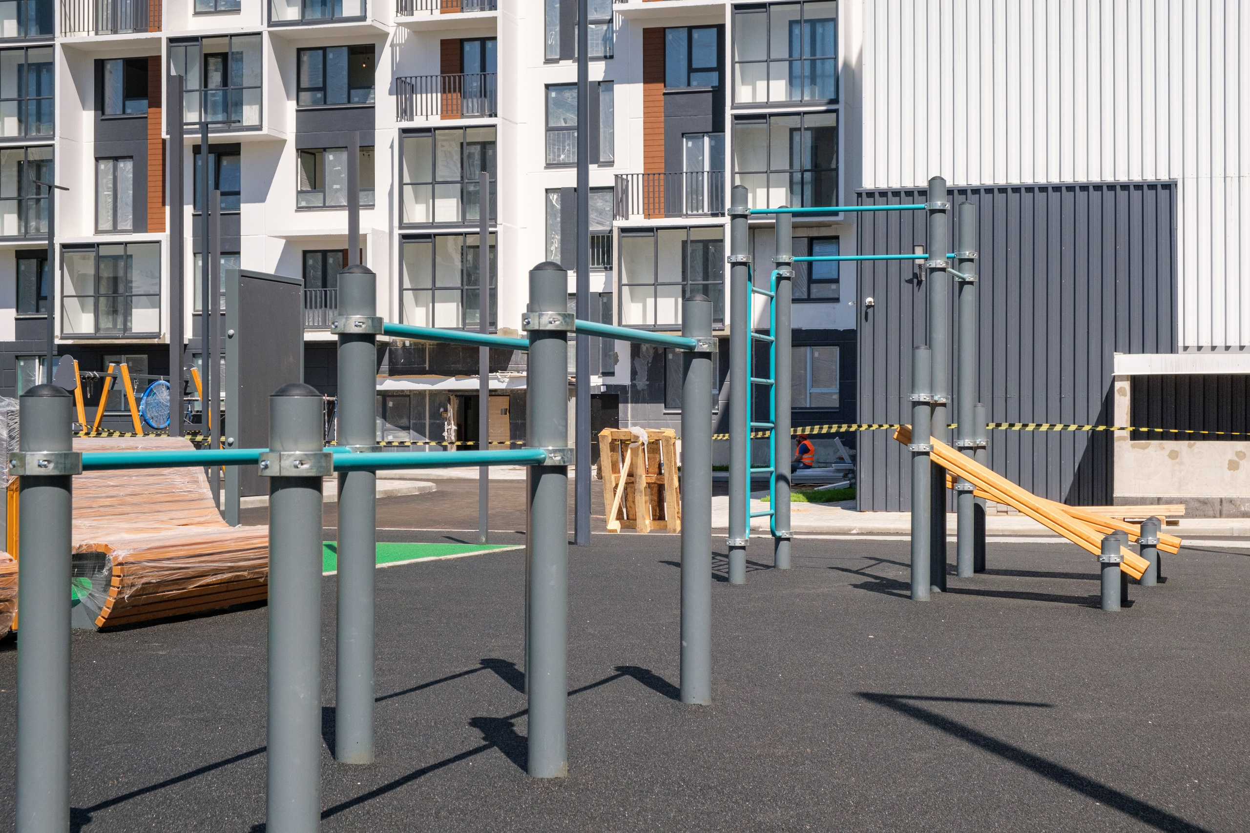 На изображении представлены детские спортивные сооружения, такие как турники и гимнастические кольца, установленные на площадке во дворе.