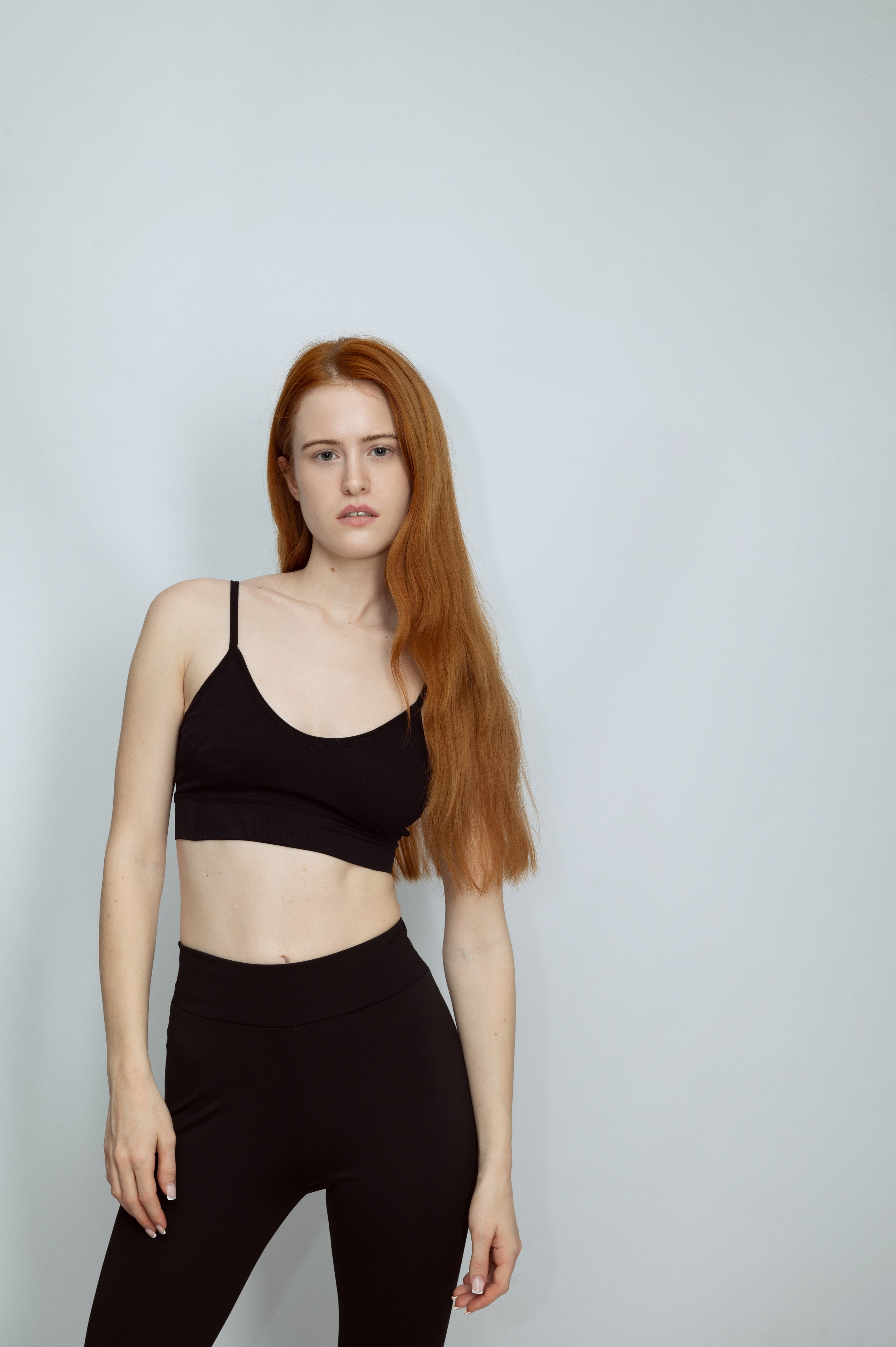 Рыжеволосая девушка-модель в черном топе и черных брюках на сером фоне. Модельные тесты