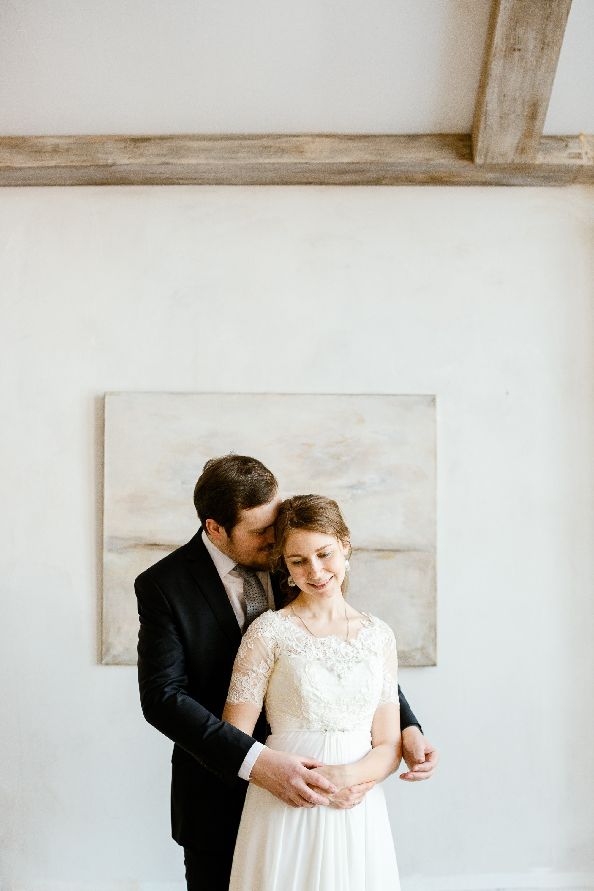 Жених и невеста в праздничной фотостудии. Жених в костюме, невеста в красивом белом платье. На фоне картина.