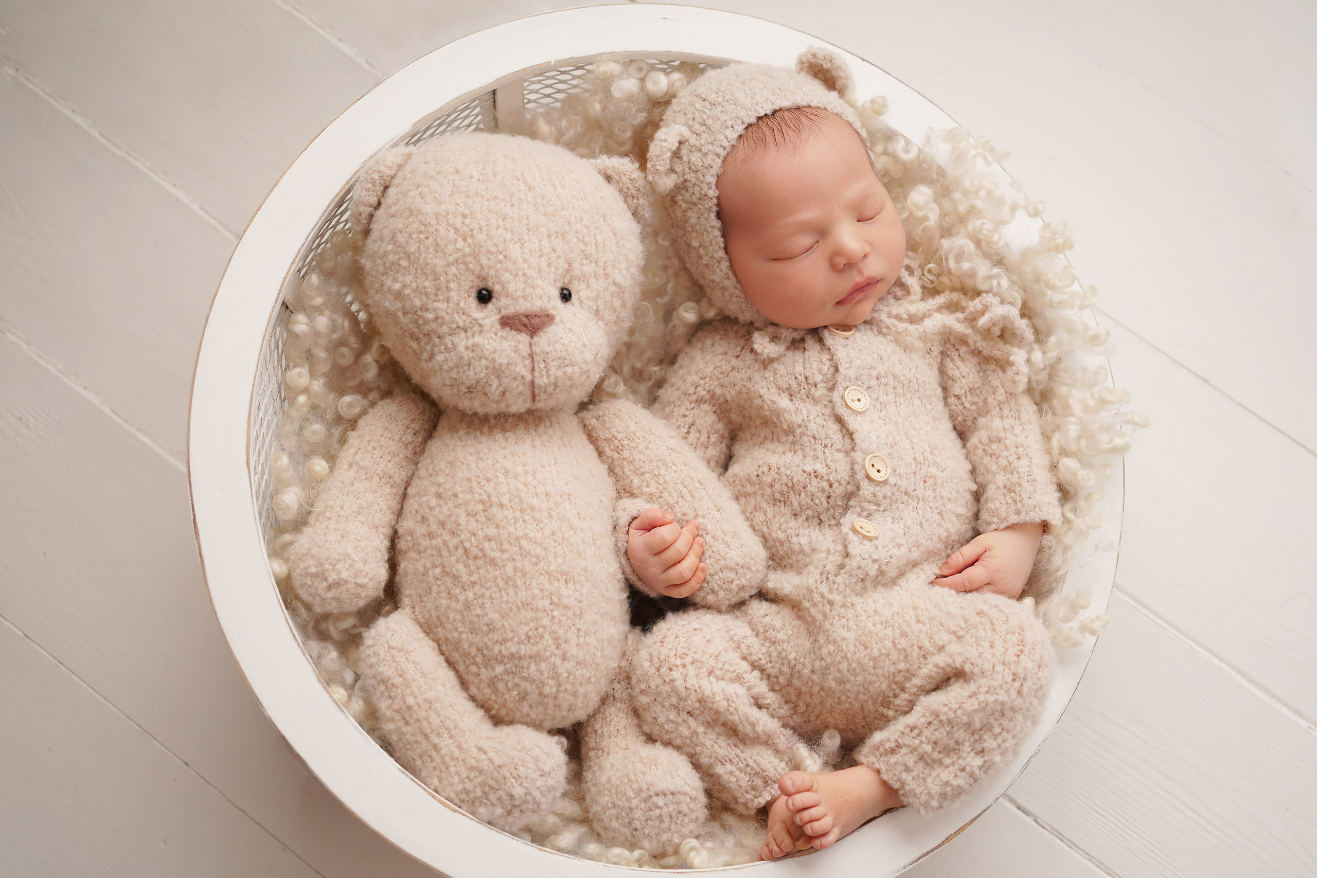 На фото новорожденная девочка в костюме мишки лежит в обнимку с большой игрушкой медведя.