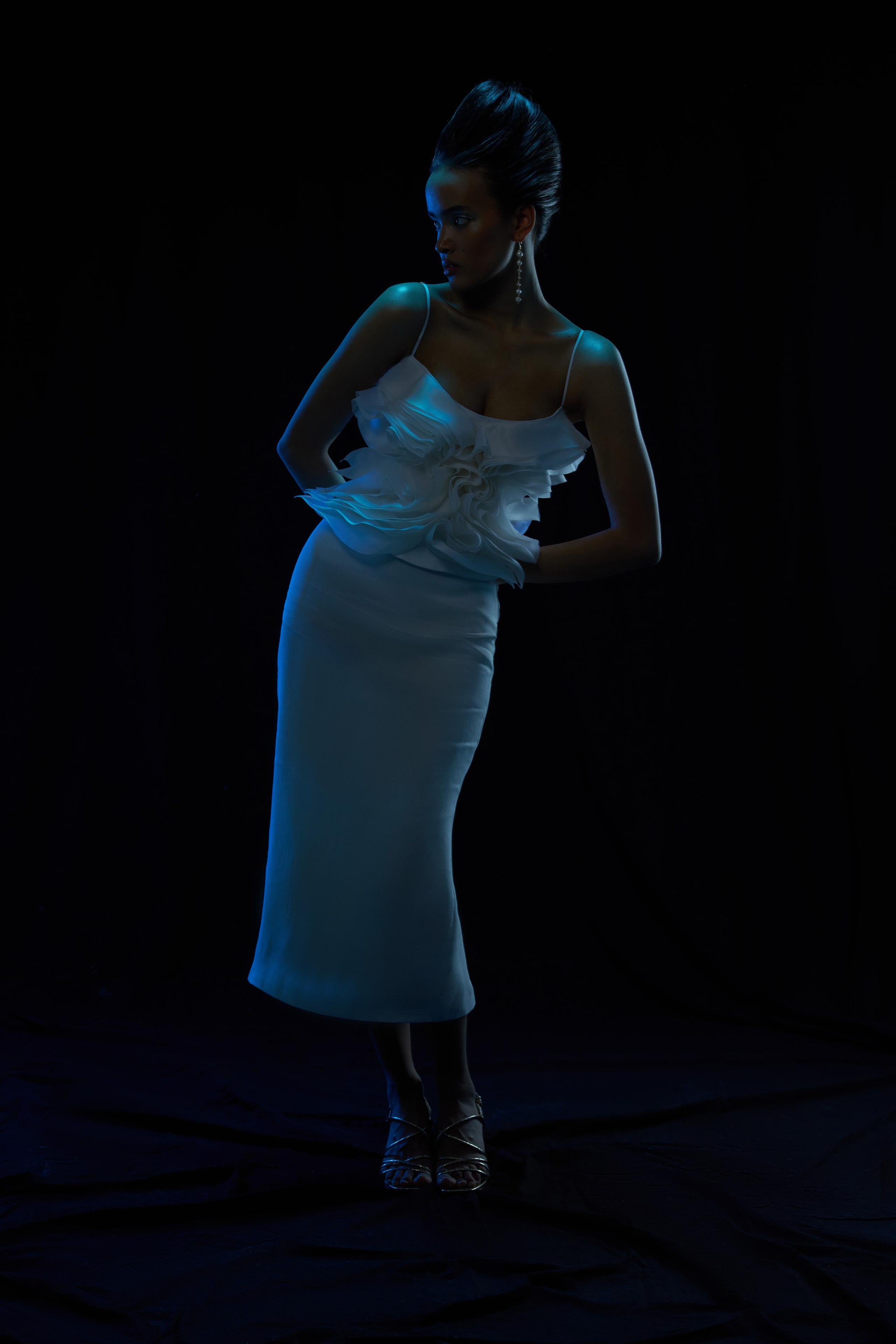 Девушка-мулатка с красивой высокой прической в белом шелковом костюме на черном фоне