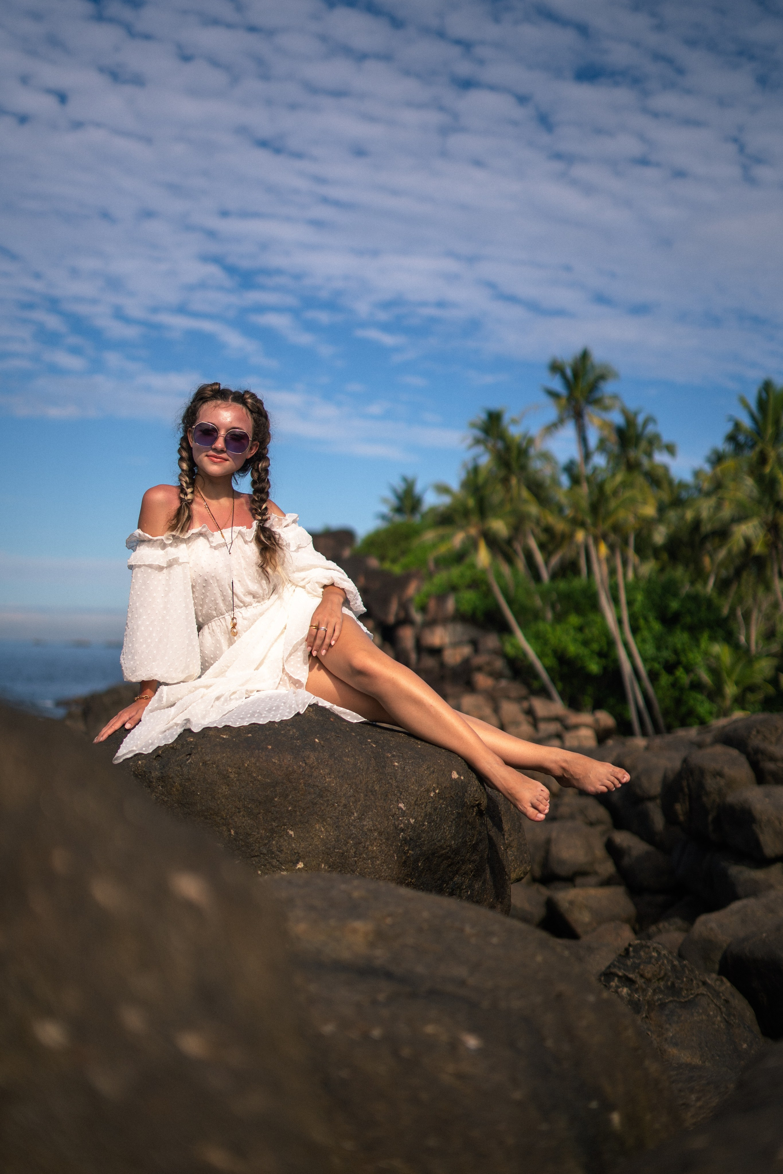 a young girl in a white dress and glasses taking steps on the rocks by the ocean